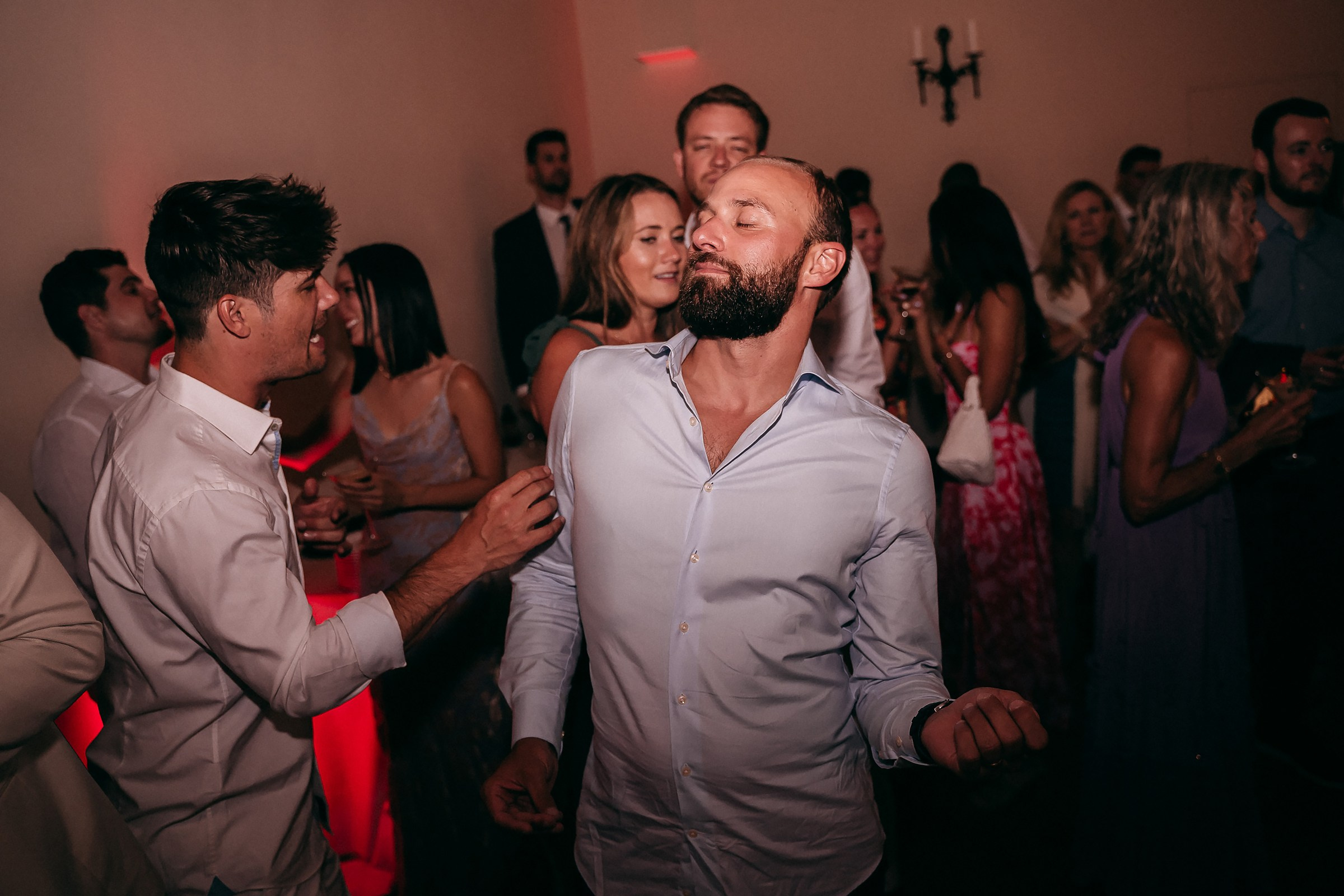 The groom dances enthusiastically in a crowded room, his relaxed pose and playful expression radiating happiness during the wedding reception.