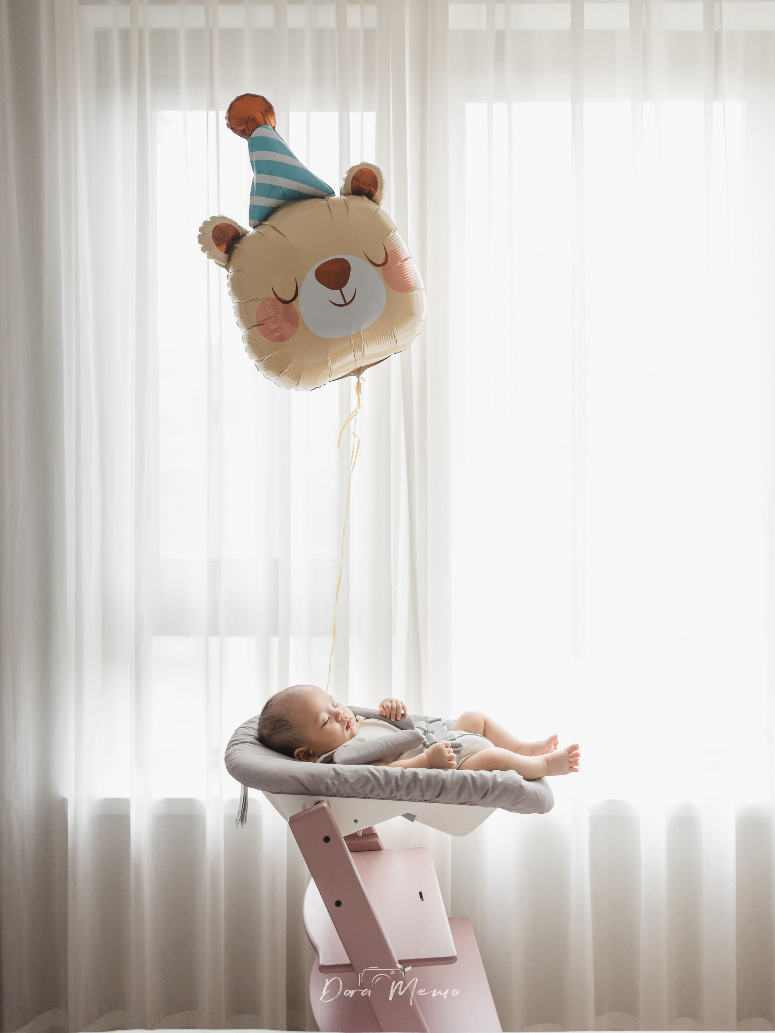 100-day baby portrait at home with a soft birthday balloon and bright window light.