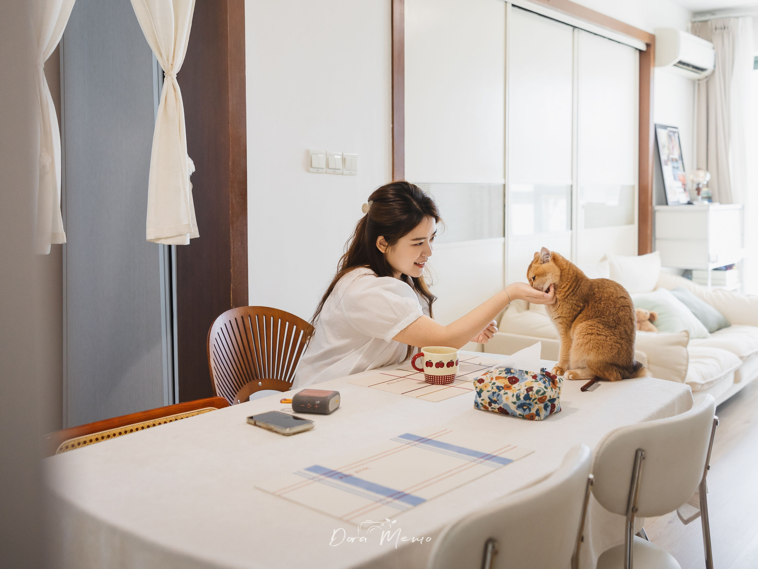 A woman reaches toward her cat across a dining table in a bright Shanghai home.