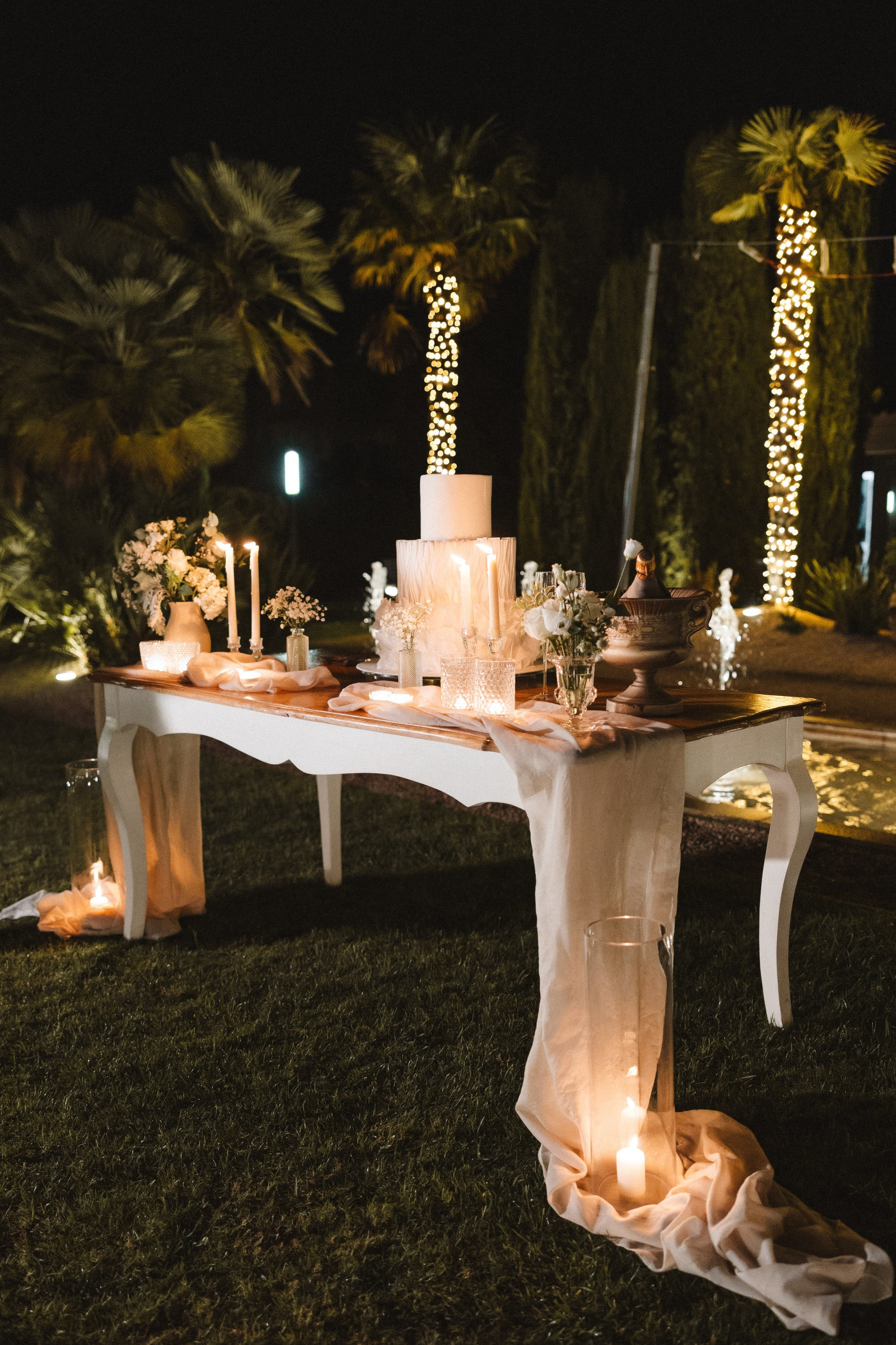 Mesa de bolo de casamento iluminada à noite com velas e arranjos florais em Famalicão.