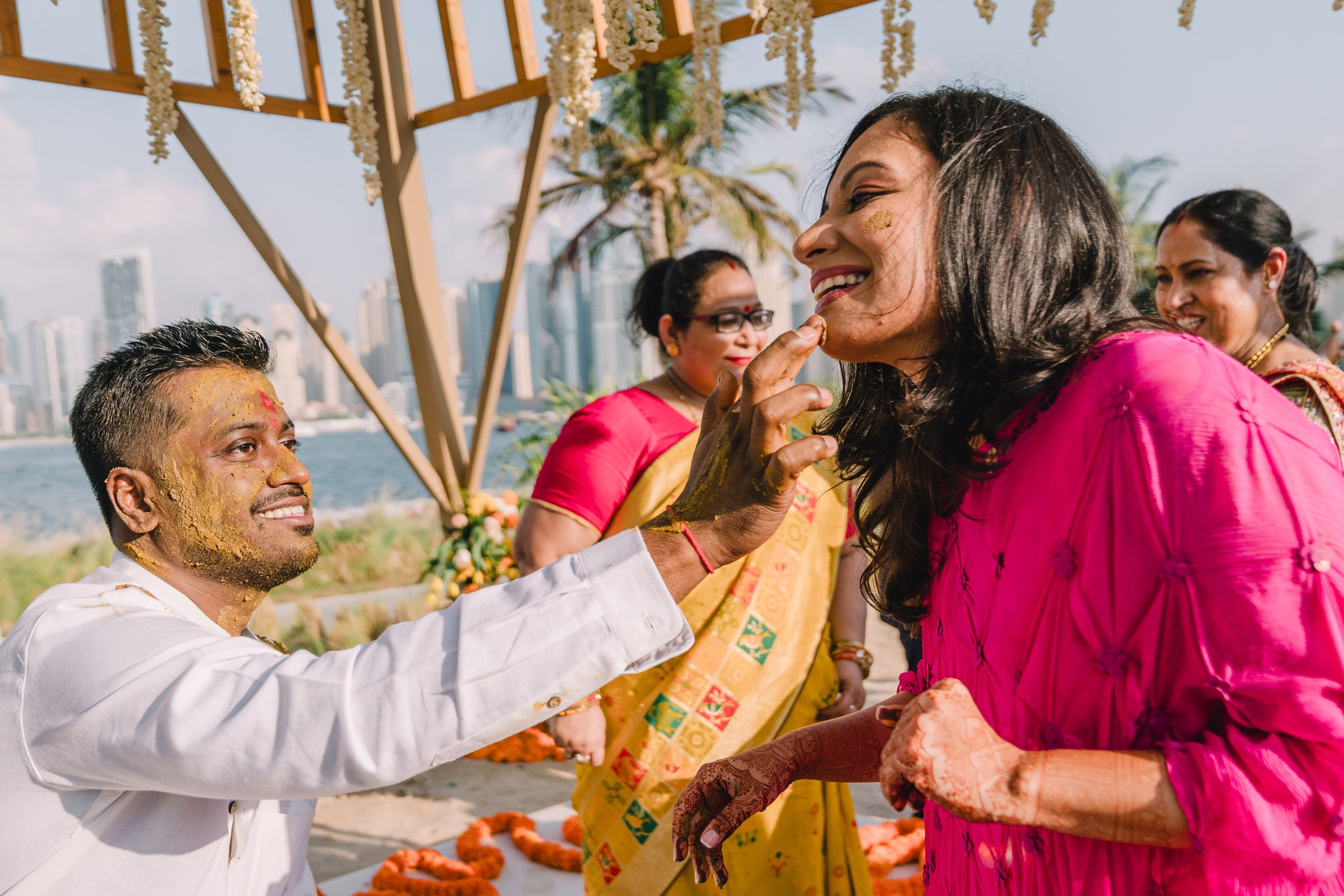 groom in a white shirt and his bride in a beautiful purple dress are touching each other and laughing