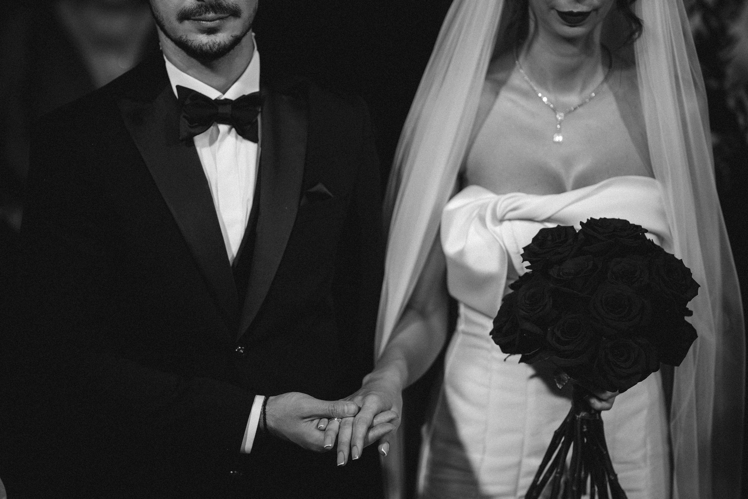 Fotografie alb-negru cu mirii ținându-se de mână în fața preotului.