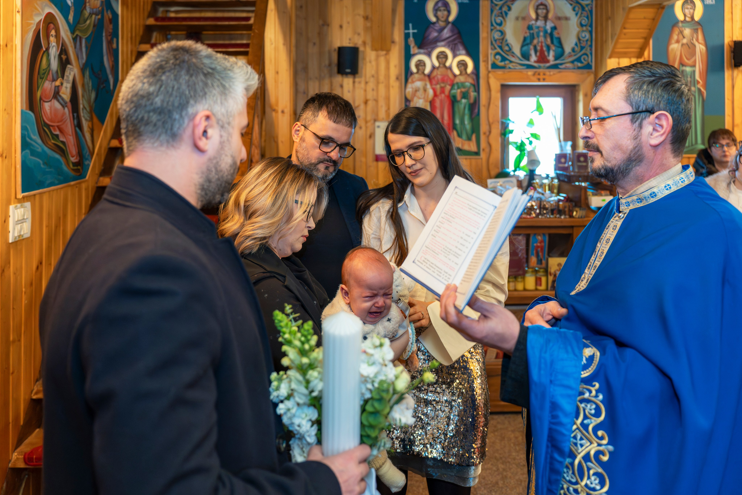 Priest reading from a book during a church baptism with family and crying baby.