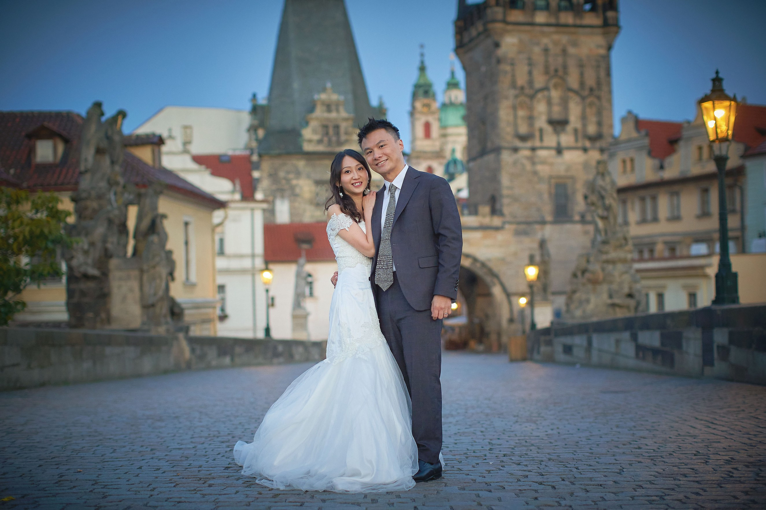 Newlyweds Eva and Conan in joyful embrace at sunrise on Charles Bridge, Prague.