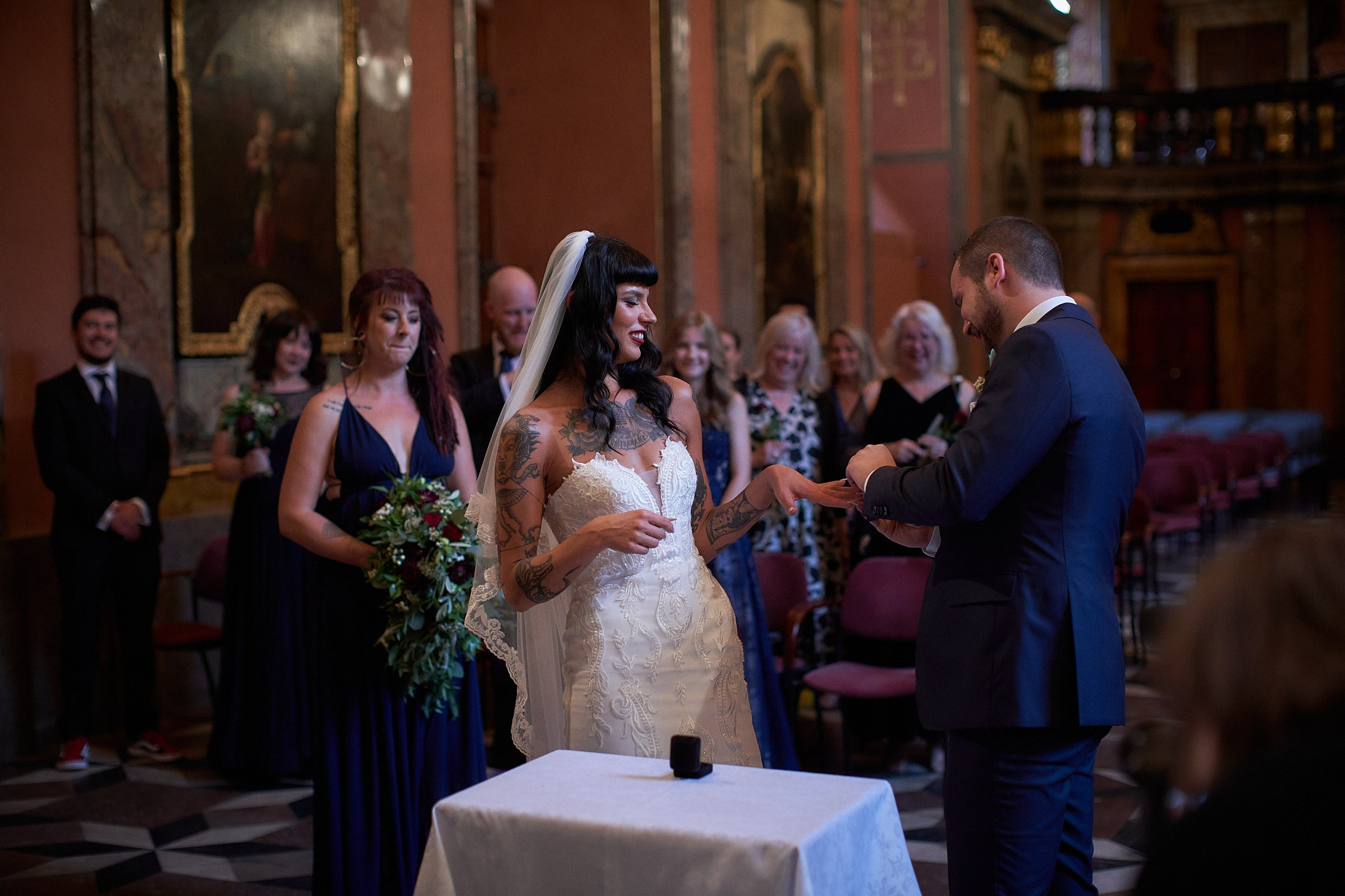 Tattooed bride offering hand for wedding band placement.
