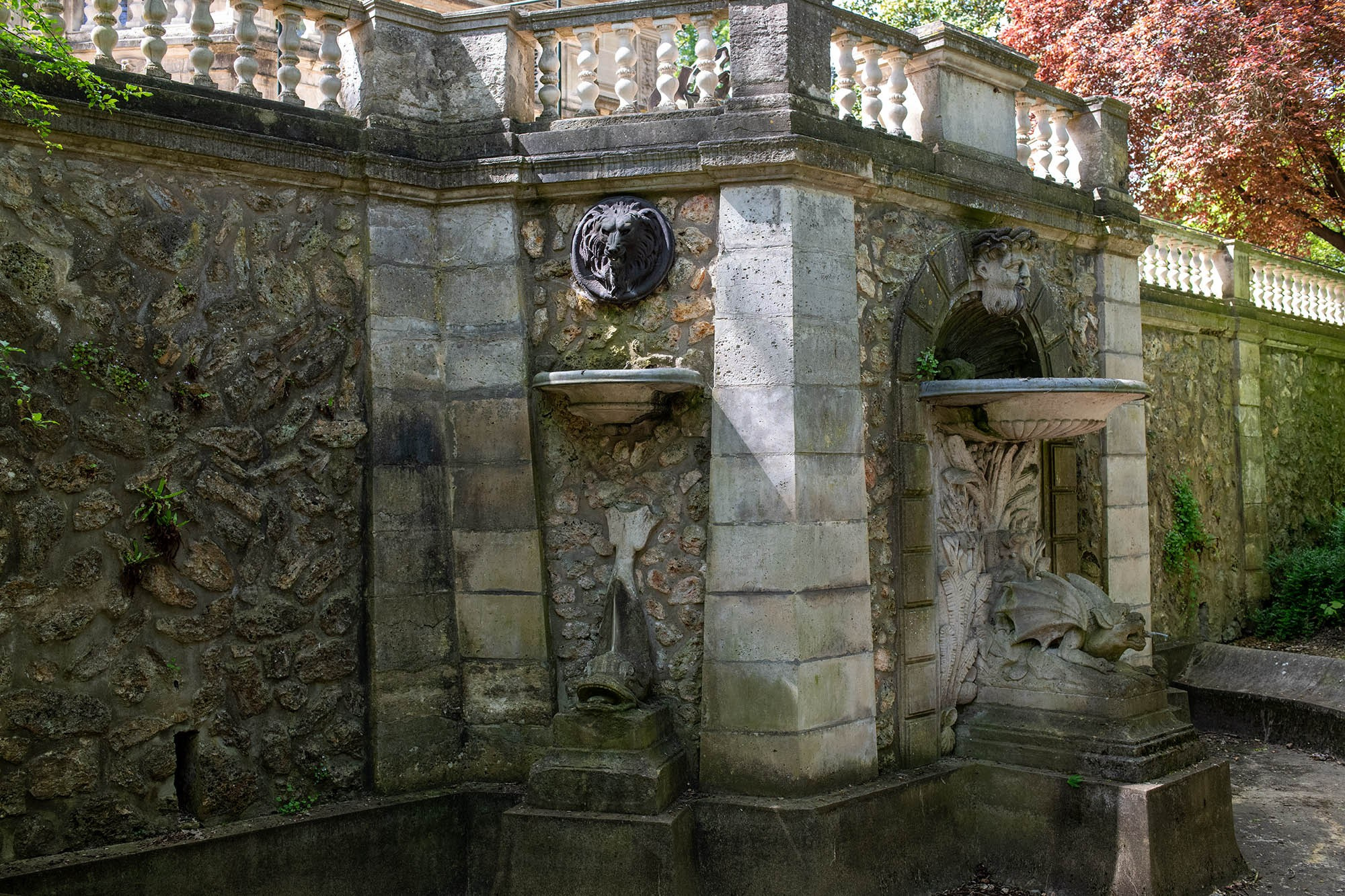 Decorative stone fountain with lion and satyr masks built into the terrace wall at the Château de Monte-Cristo in France.