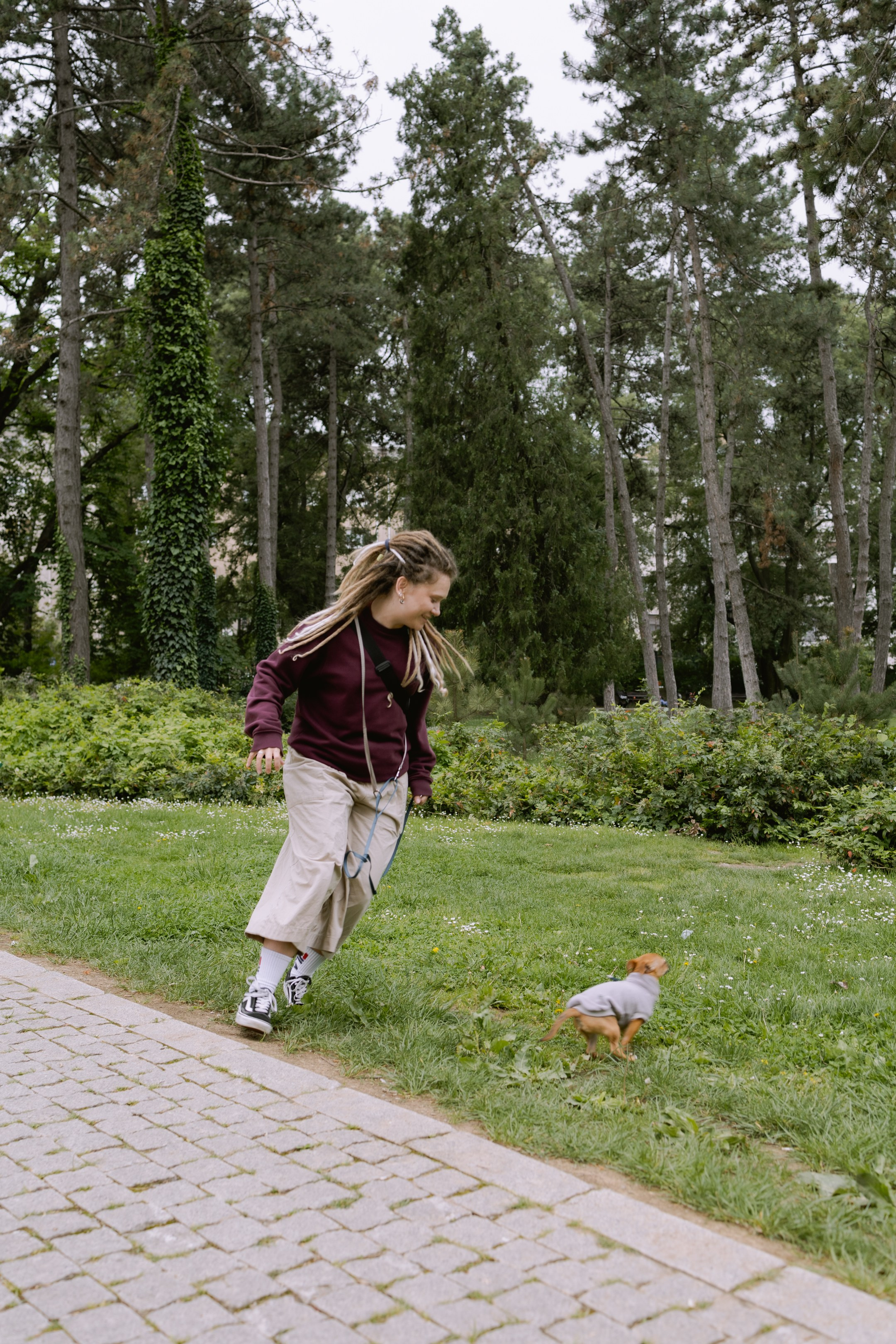 Юля с радостью бежит за той-терьером Роки по зелёному газону в парке.