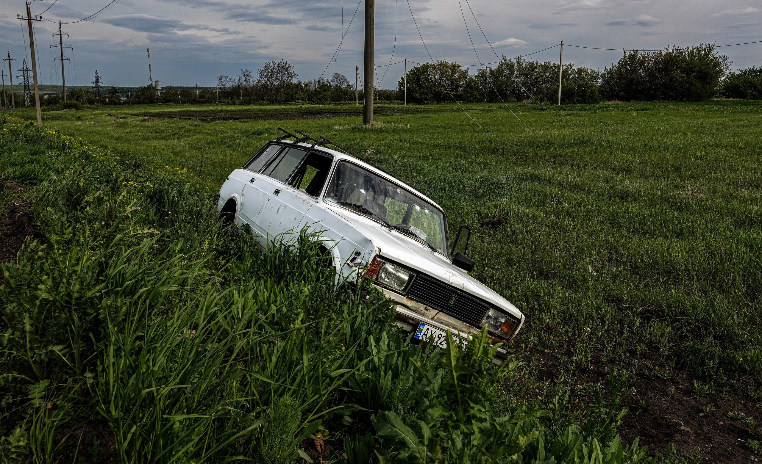 Une voiture de civil sortie de route, avec des impacts de balles visibles sur le pare-brise, près de Kharkiv.