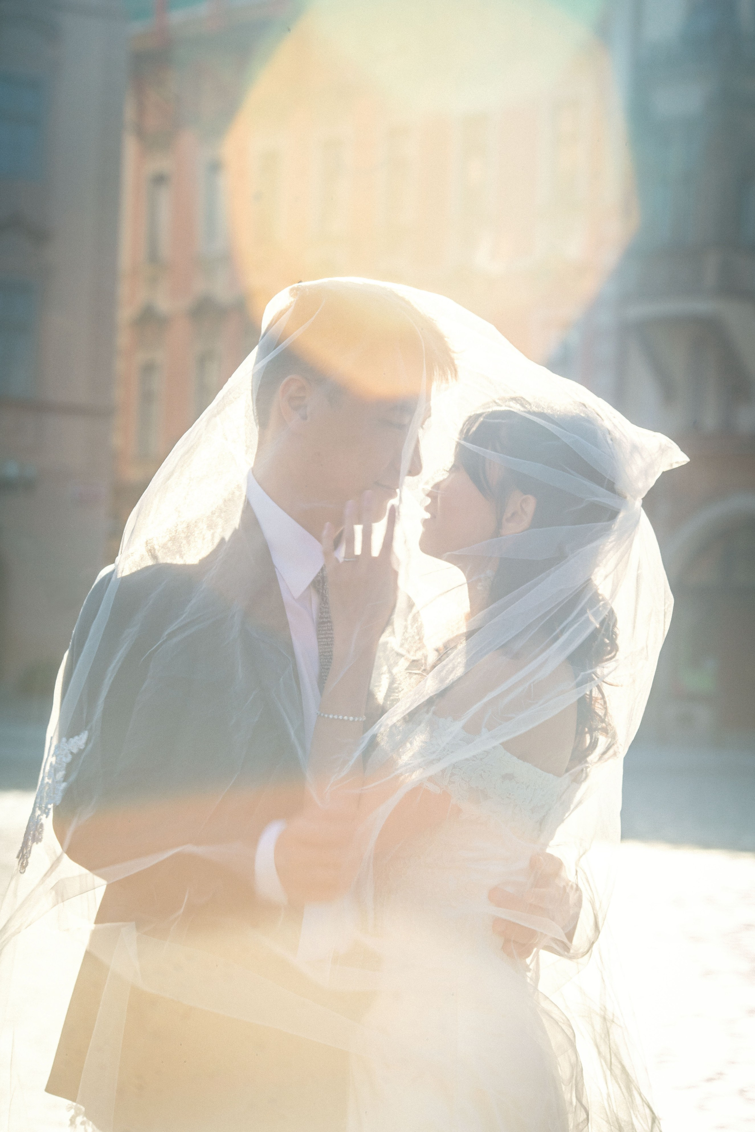 Eva caressing Conan’s face under a veil with lens flare and sunrise light in Old Town Square.
