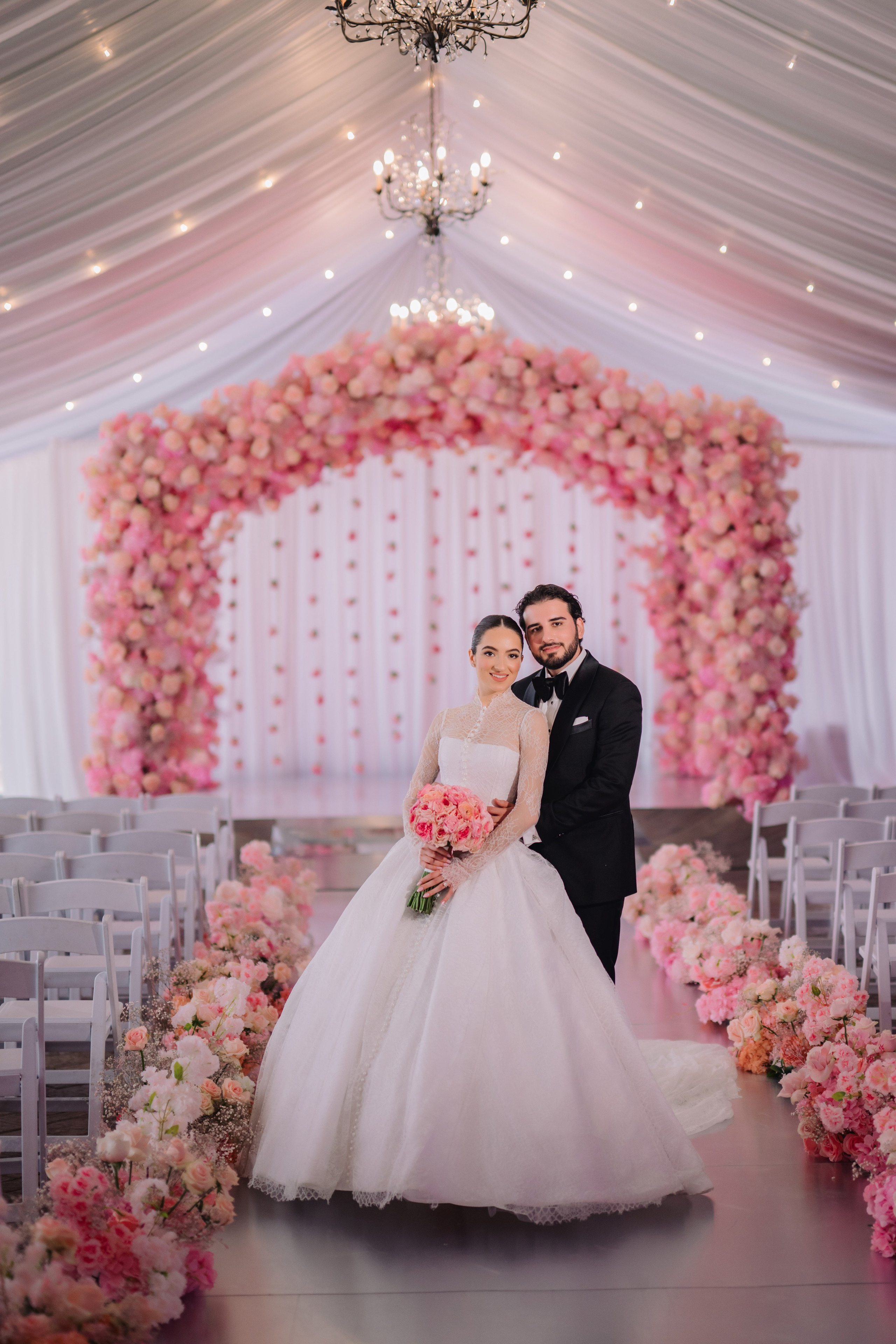 a bride and groom pose for a photo in front of a floral arch