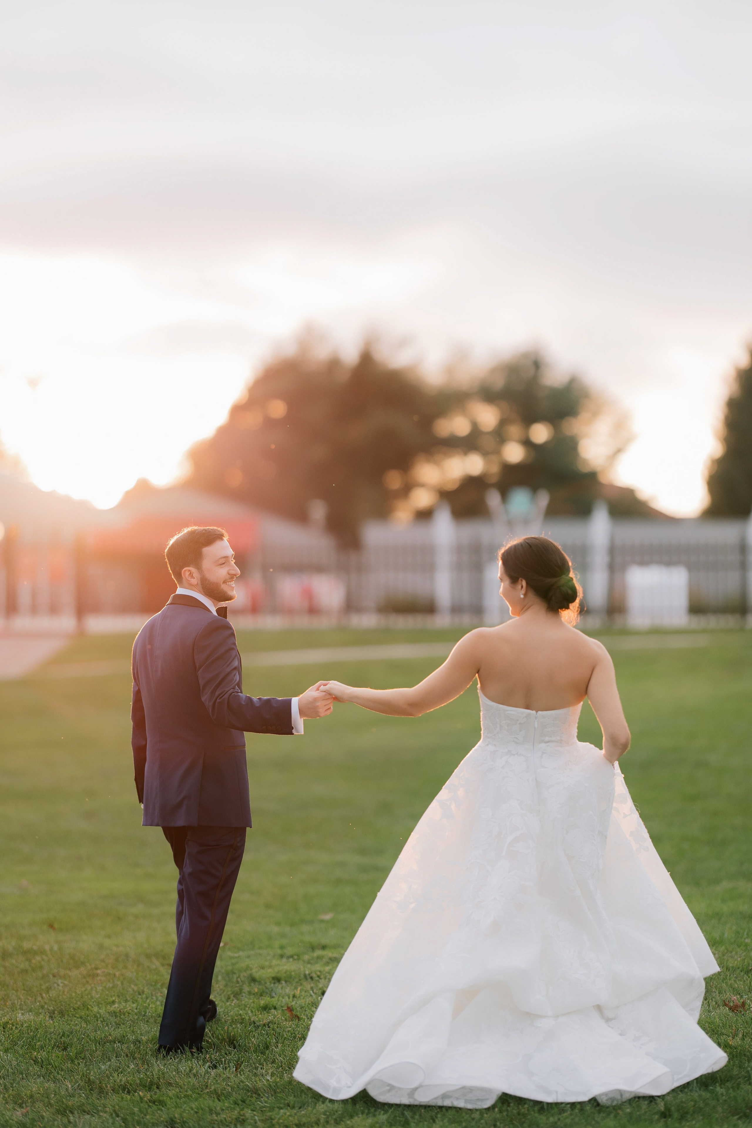 a bride and groom walking through the grass at sunset