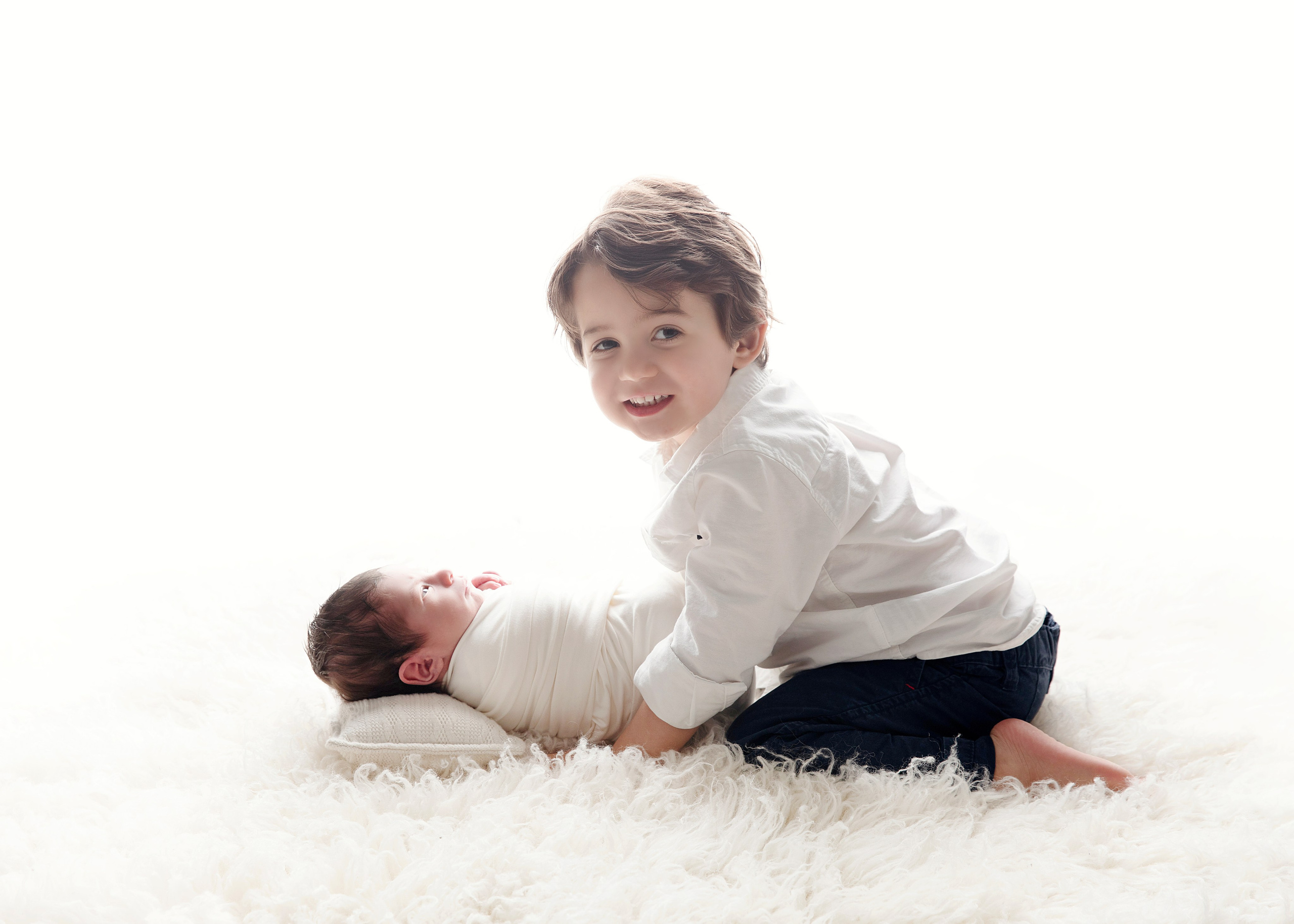 "Nyfödd bebis som ligger i knäet på sitt äldre syskon. Bilden visar den speciella relationen och ömheten mellan dem och passar utmärkt för att framhäva familjeband i nyfödda fotograferingar."