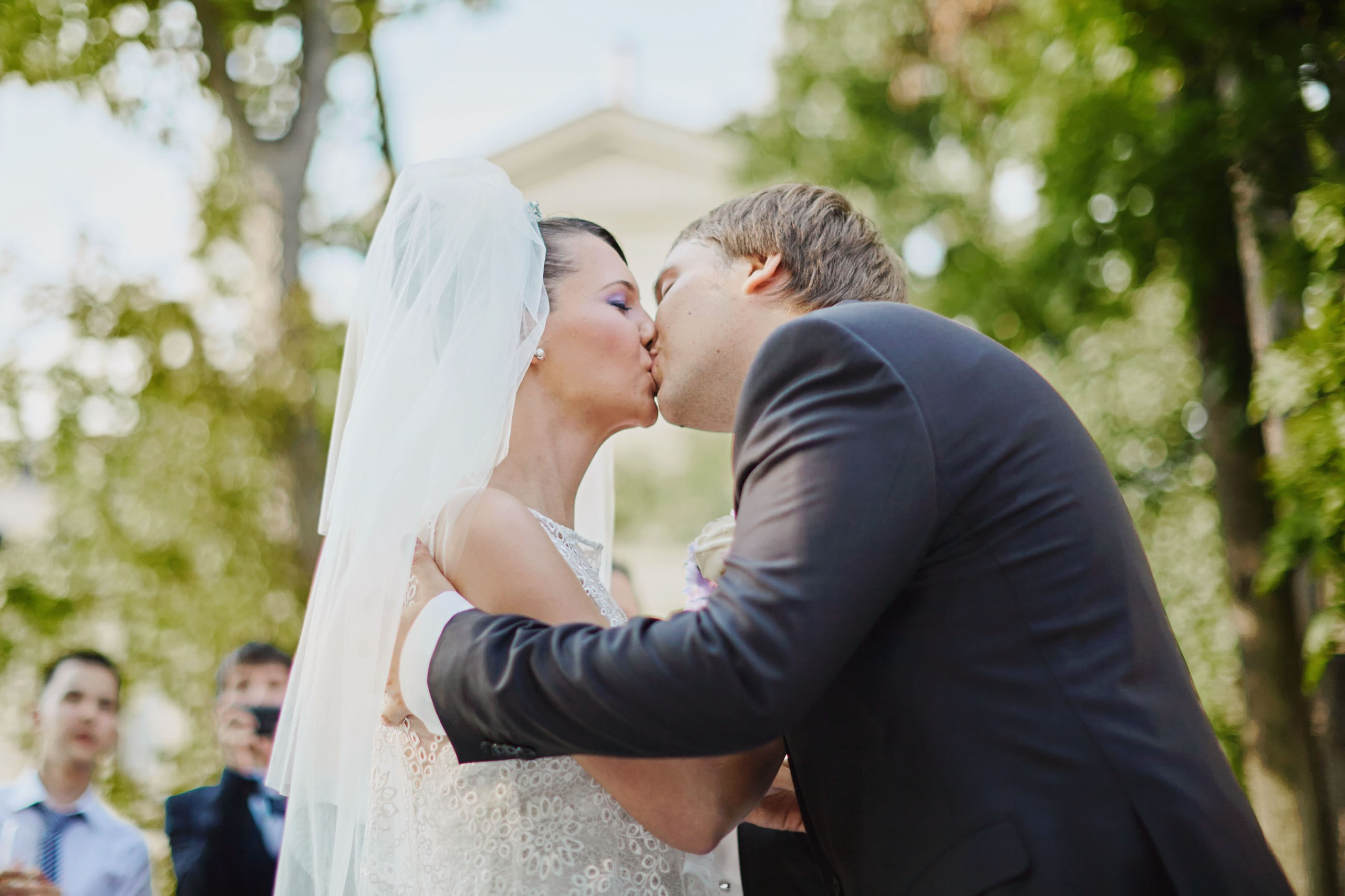 Newlyweds' first kiss at outdoor wedding with family and friends.