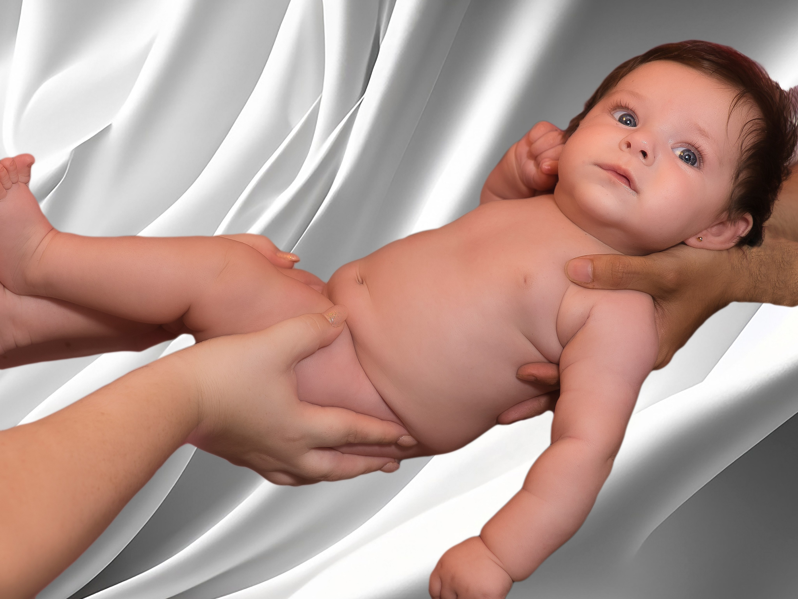 Niña vestida con traje de bautizo blanco, sostenida por sus padres en la iglesia.