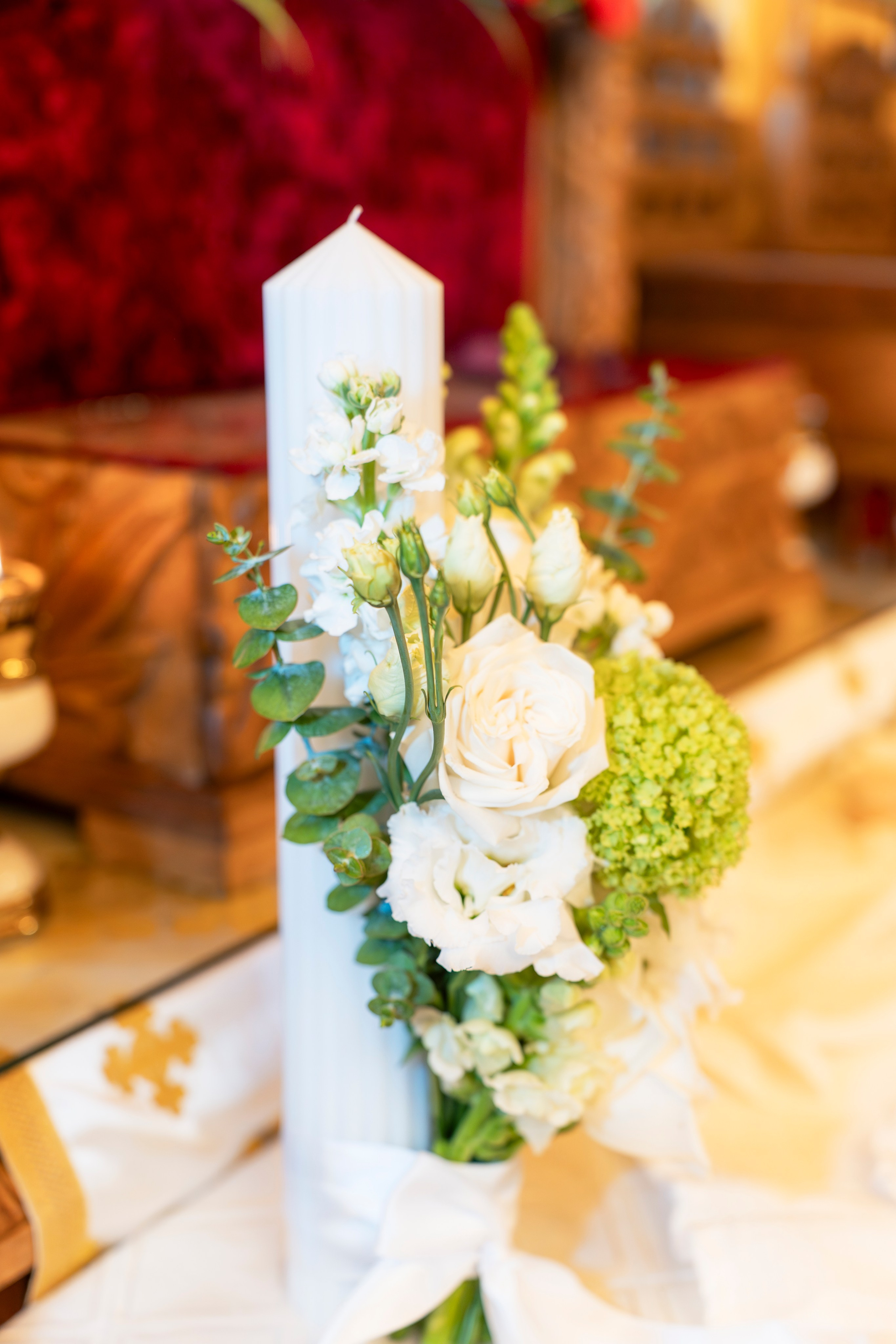 White candle decorated with white and green floral arrangement tied with a white ribbon.