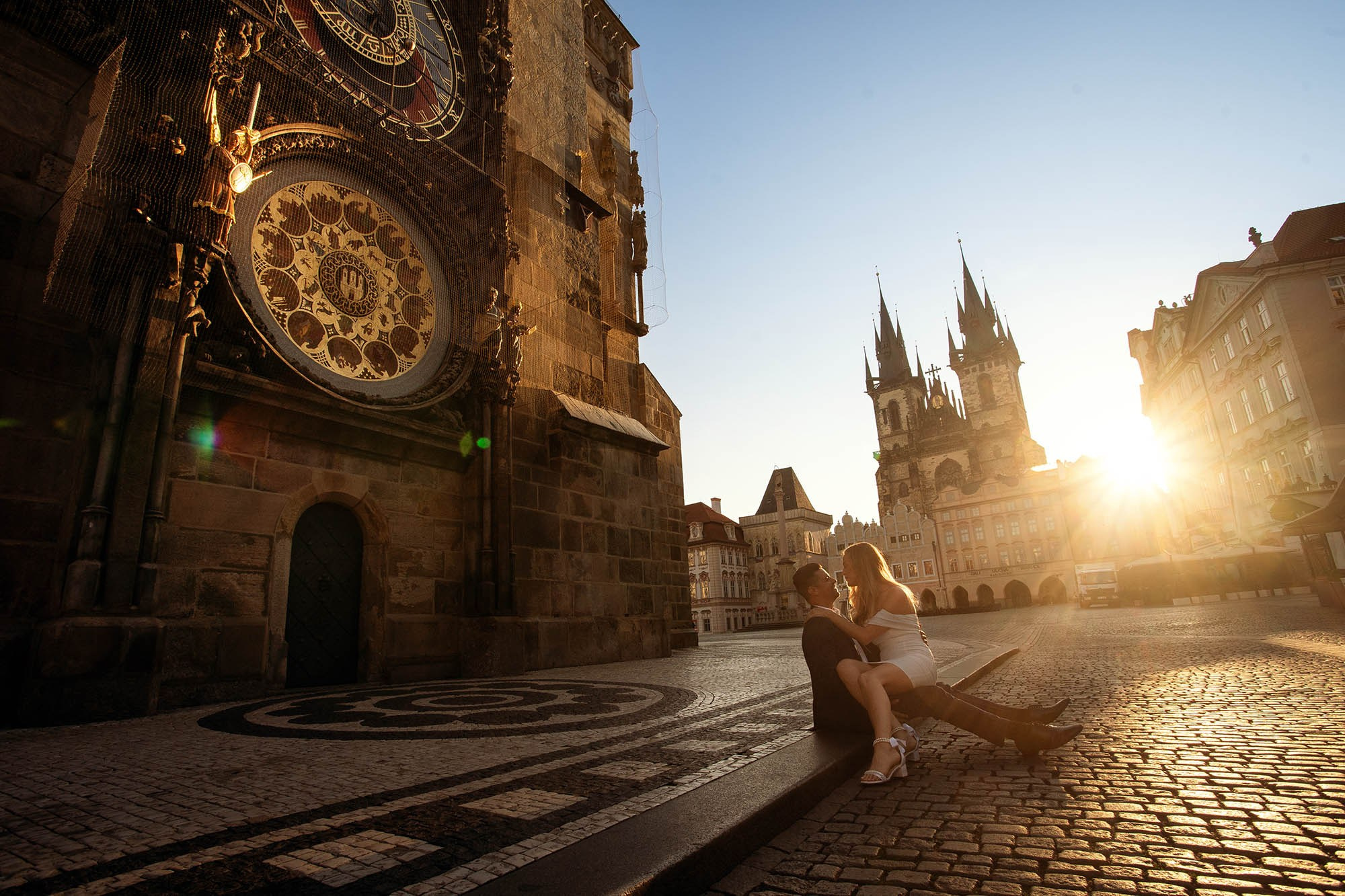 A couple sitting under the Astronomical Clock bathed in the Prague sunrise glow.