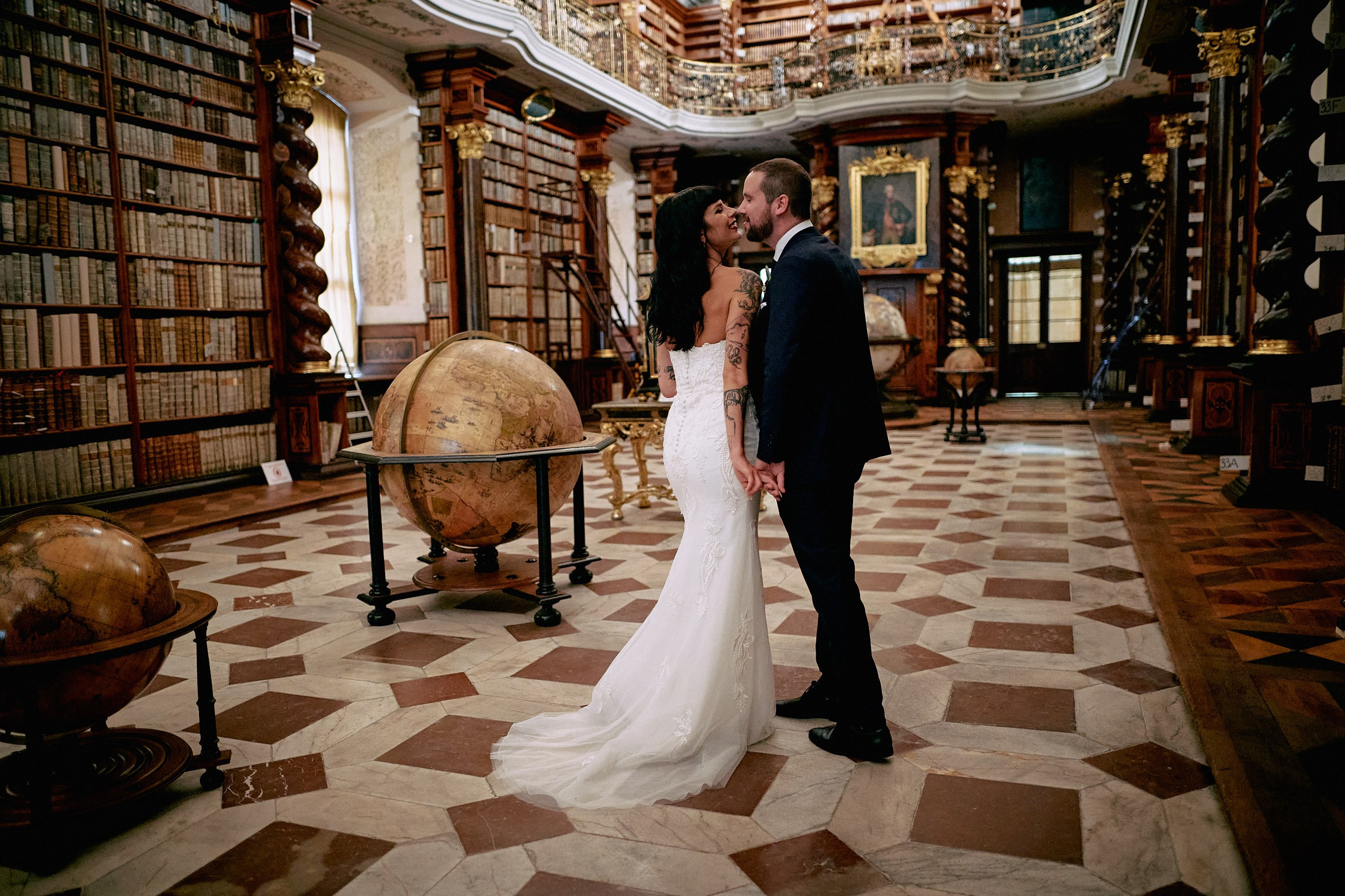 Newlyweds sharing romantic hug in priceless Klementinum Library interior.