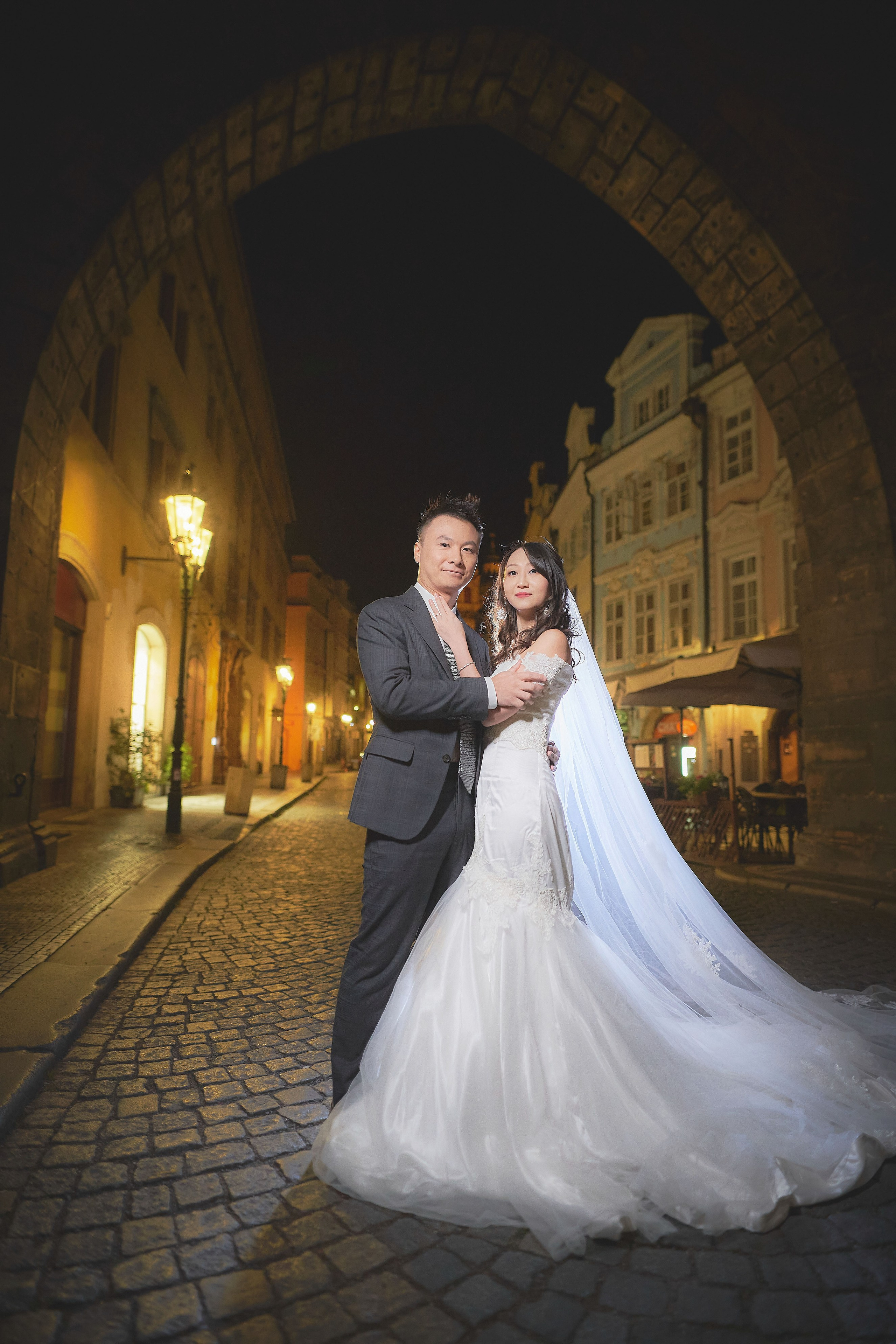 Newlyweds Eva and Conan standing hand in hand under the gothic tower arch in Malá Strana at dawn, Prague.