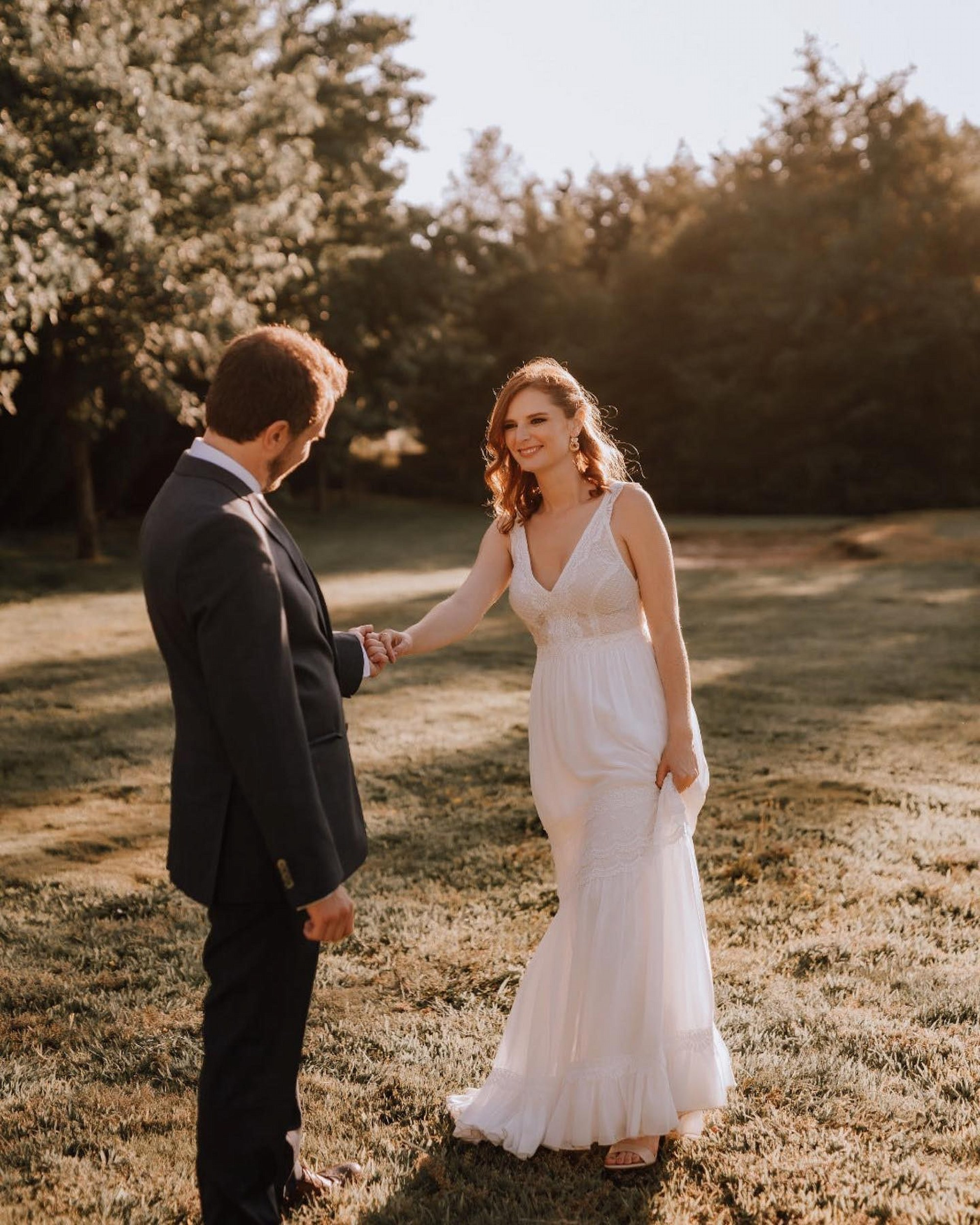 Noivo oferece a mão à noiva num jardim iluminado, captando a cumplicidade do primeiro olhar.