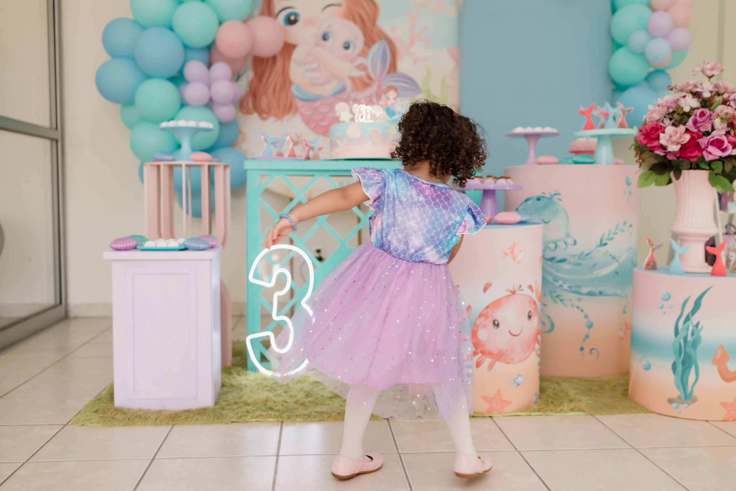 Elisa brincando de bailarina com roupa de sereia em frente a decoração da festa