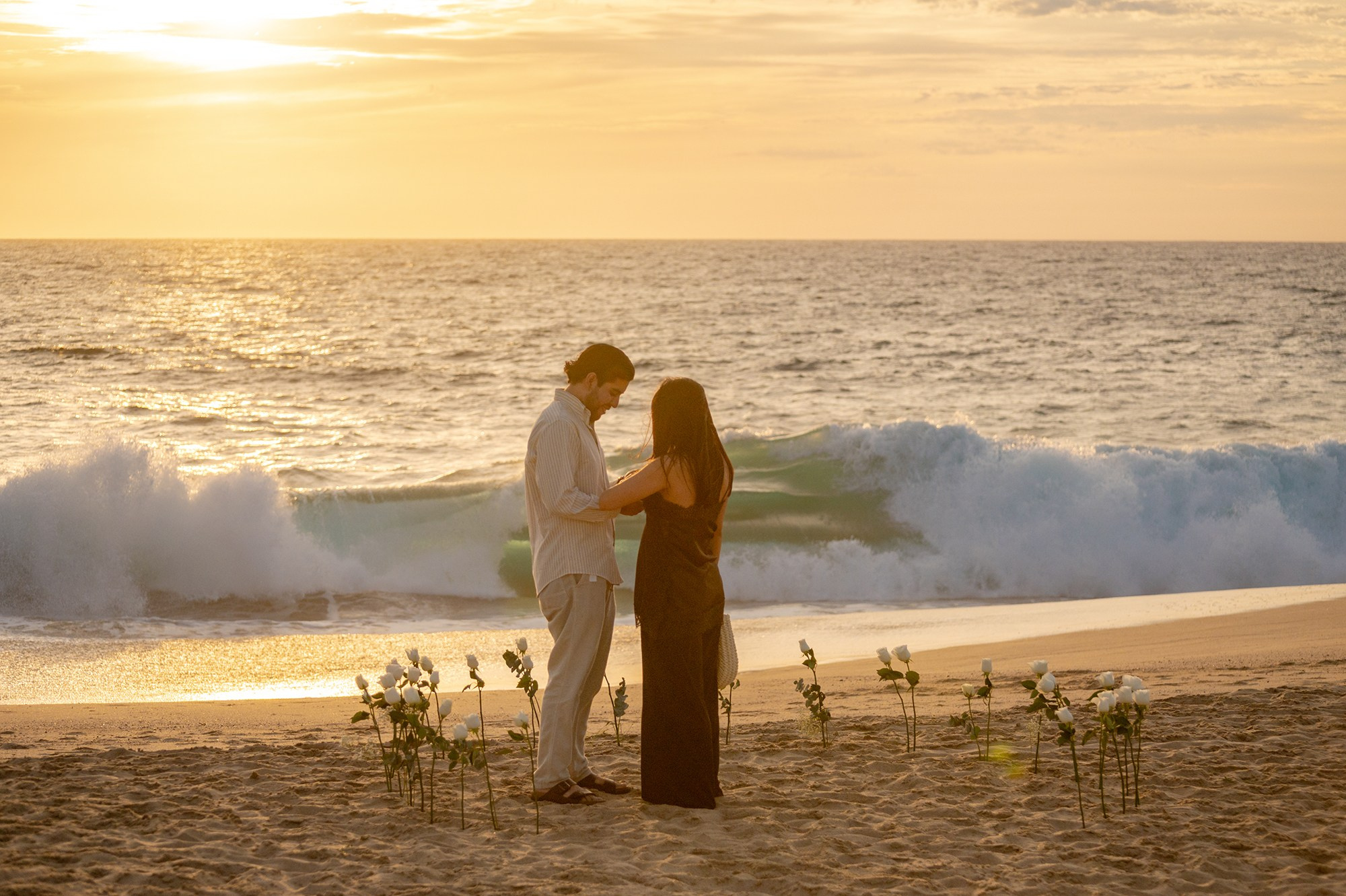 Groom putting engagement ring on bride during surprise beach proposal Los Cabos