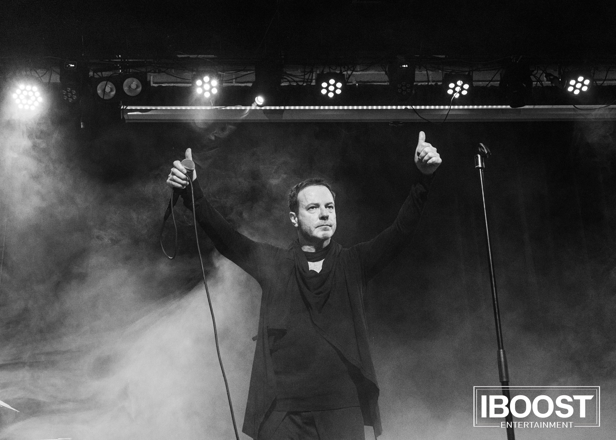 Black-and-white concert photo of vocalist Krasovitsky standing in smoke with both hands raised on stage in Sofia.