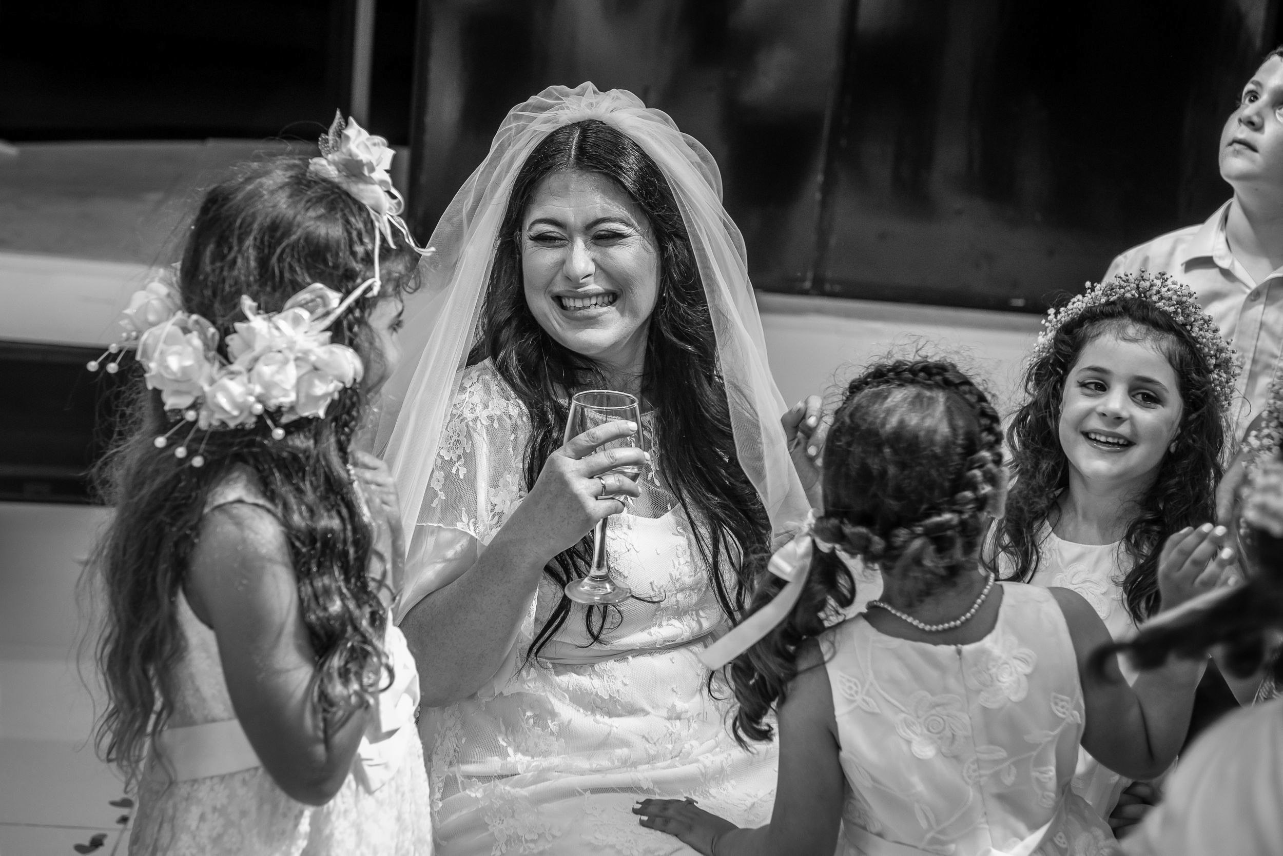A bride holding a wine glass laughs with children during the celebration