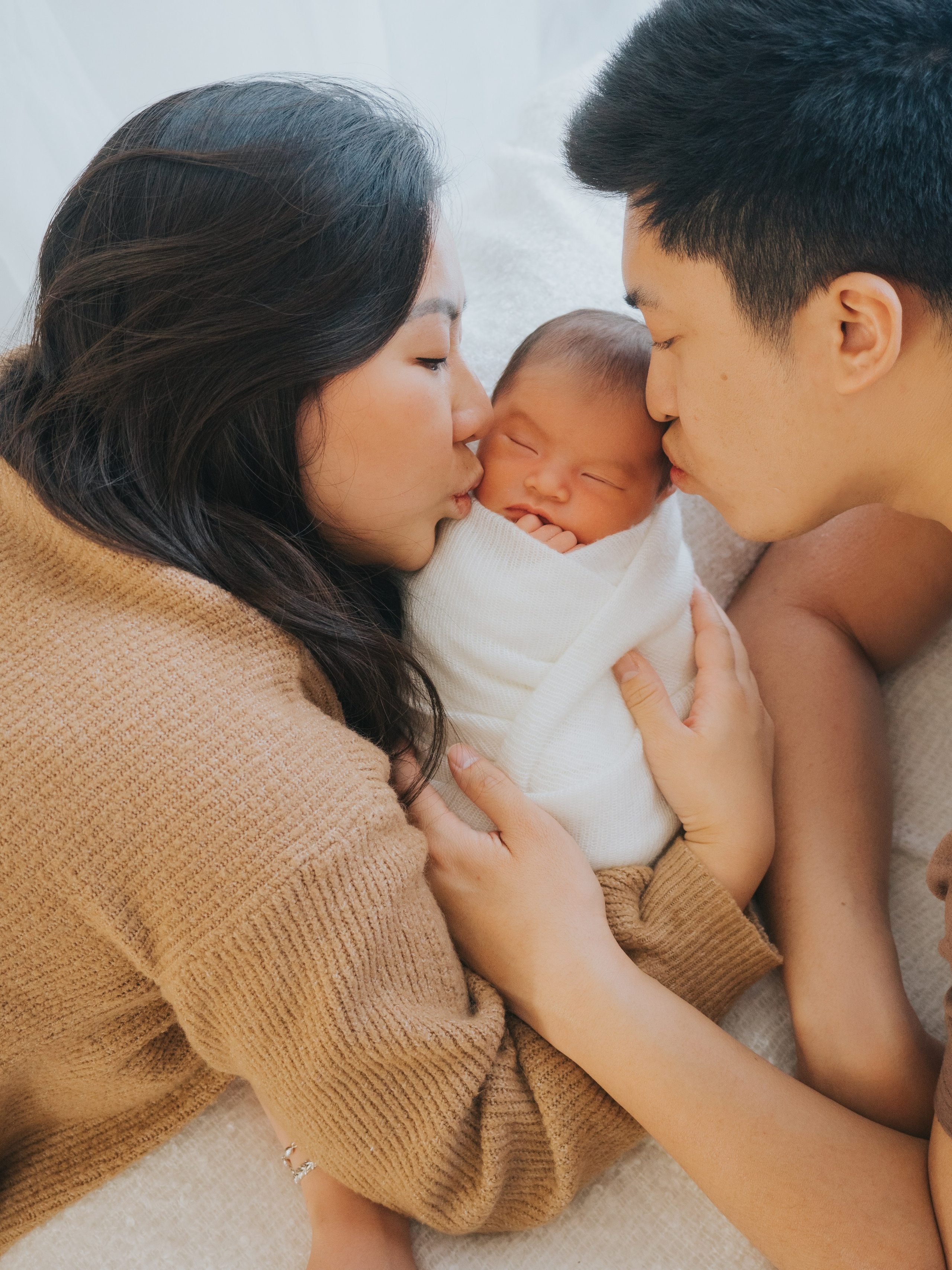Mother and father giving kiss to newborn on each side.