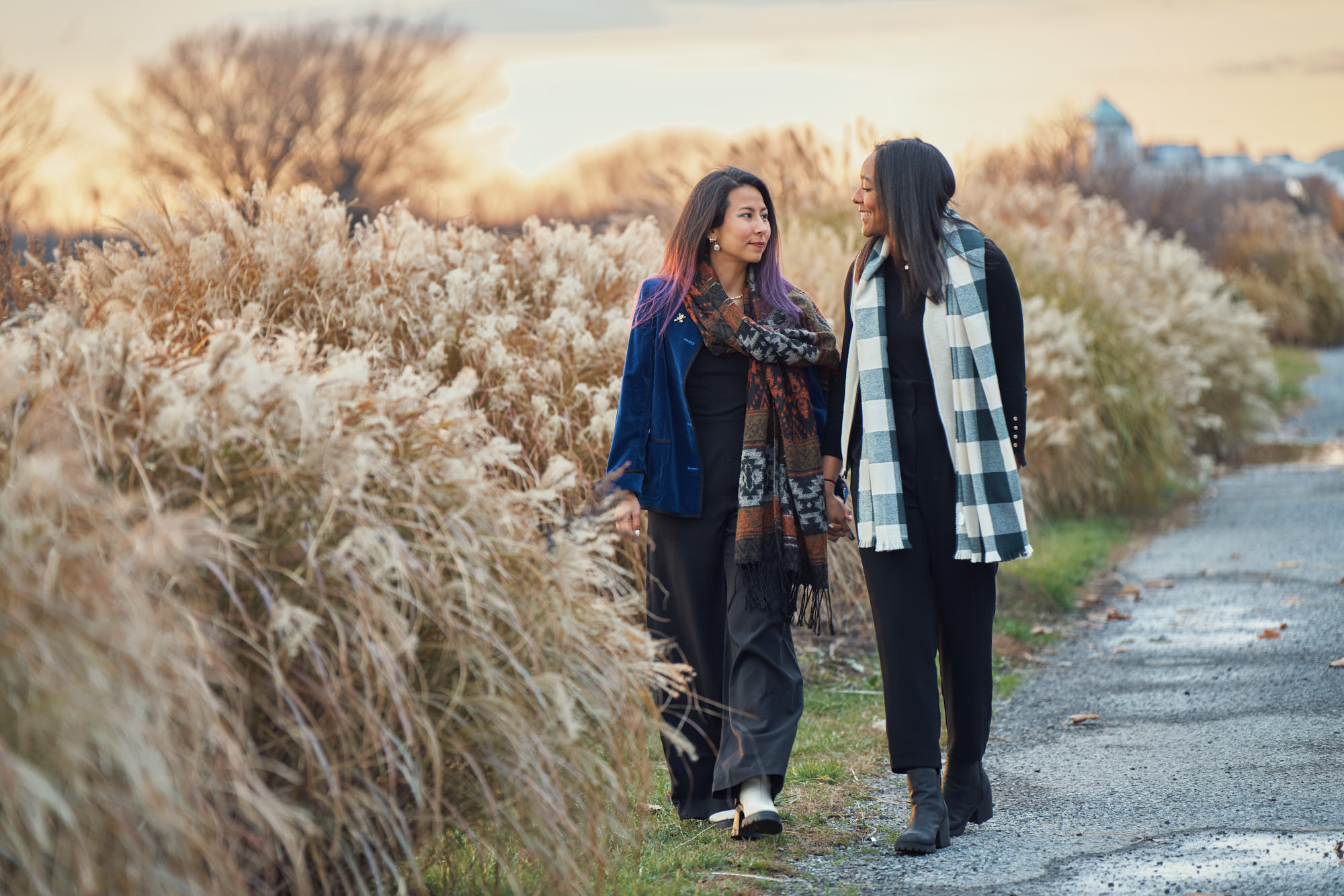 Romantic fall engagement photo of same gender female couple walking down the road and chatting. Shot during sunset in Liberty State Park, Jersey CIty, NJ.