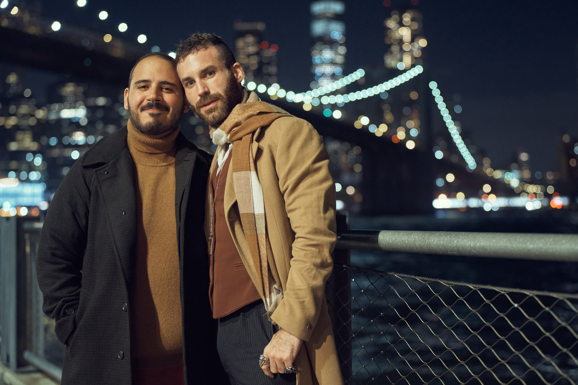 Night engagement photo of gay couple in Dumbo with iconic view on Brooklyn Bridge and Manhattan.