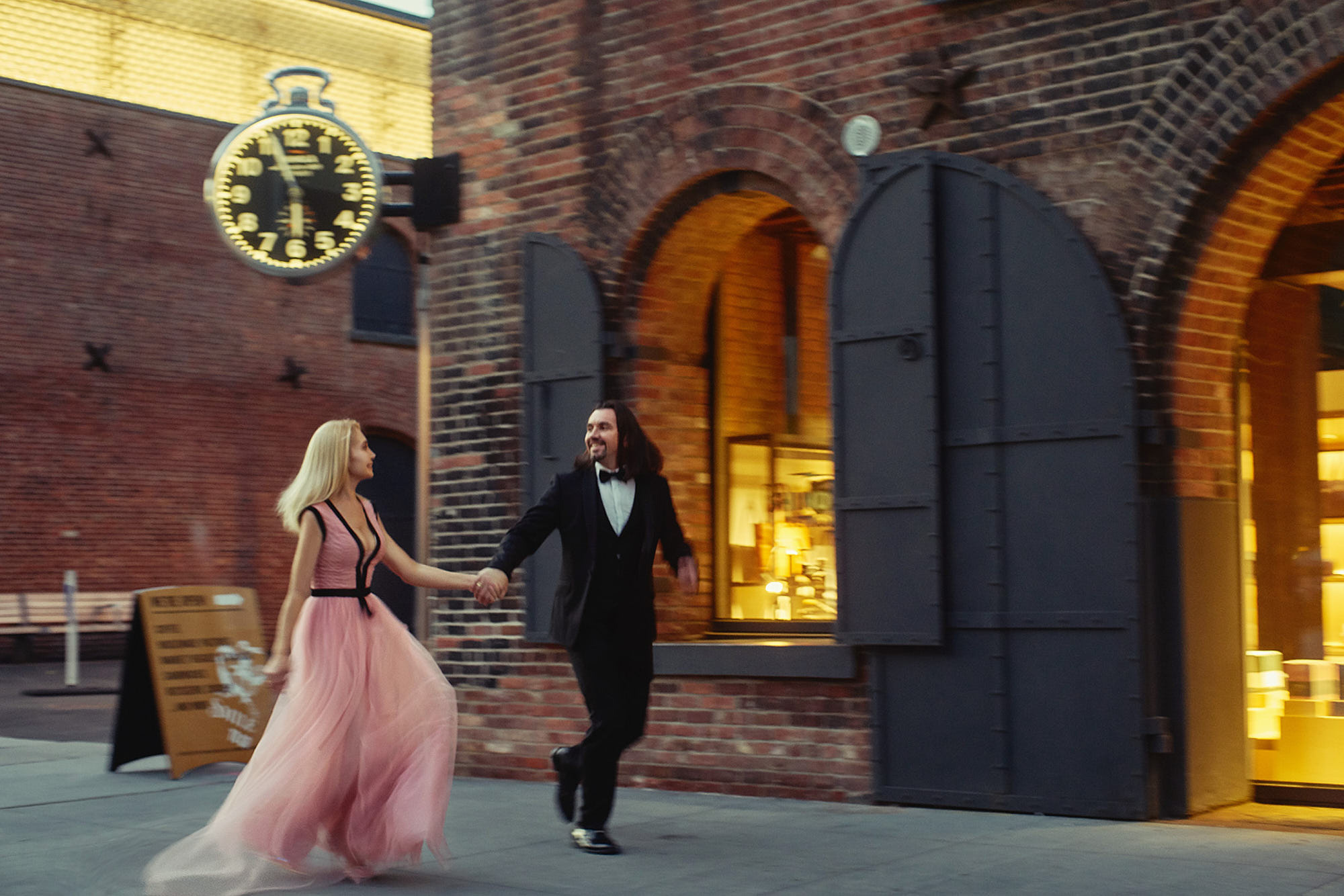 Best engagement photographer Alex Pedan shot slow motion of running couple in Dumbo with a big clocks above them.