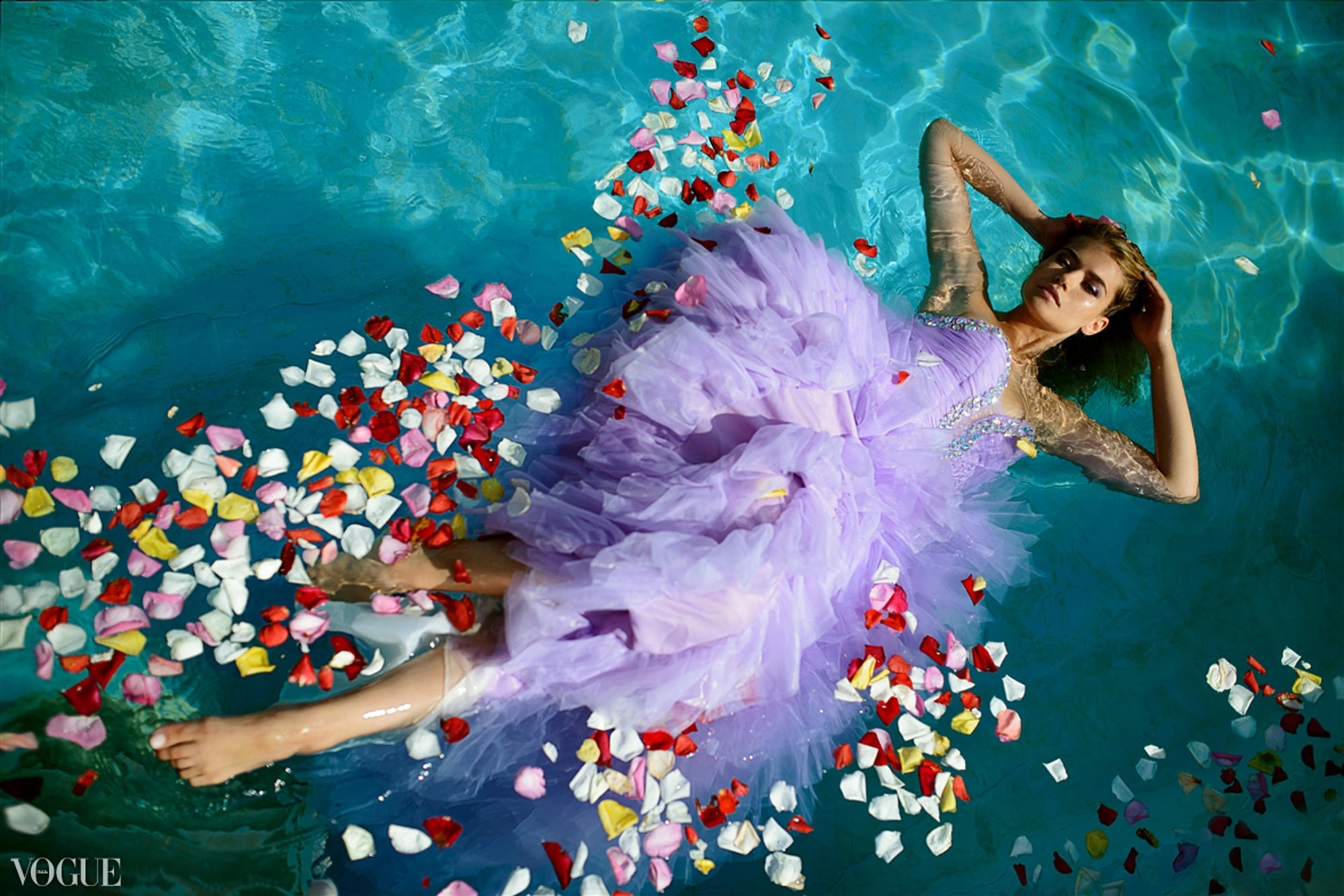 Blond model in lavanda color wedding dress swimming in the pool with roses. Editorial shot by best Miami photographer. Vogue Italia featured.