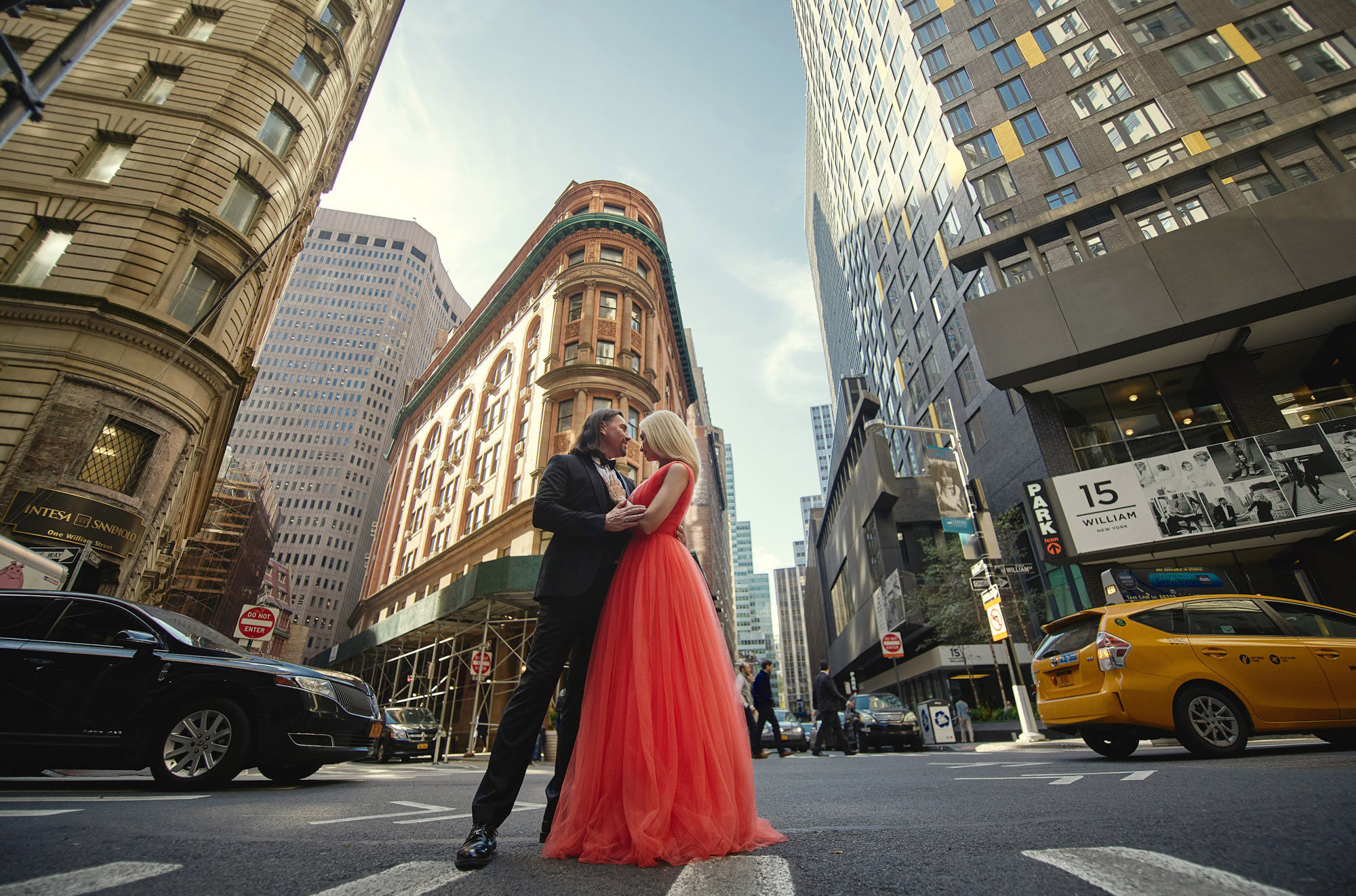Manhattan downtown engagement photo of Alex in black suit and Tatyana in red dress holding each other on the William St, New York, NY.
