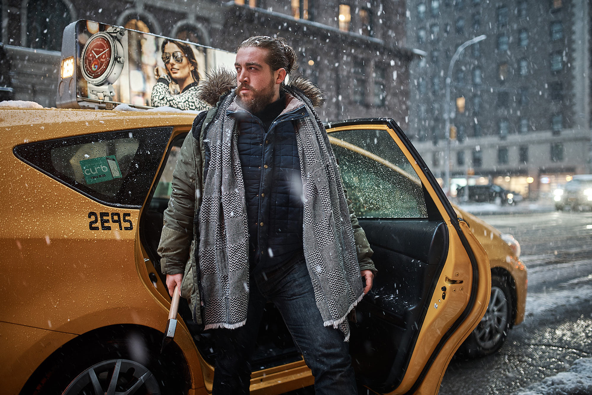 Bearded Alex Frankel with scarf in snow storm comming from a yellow cab in Manhattan, New York holding Husky Axe. Editorial shot.