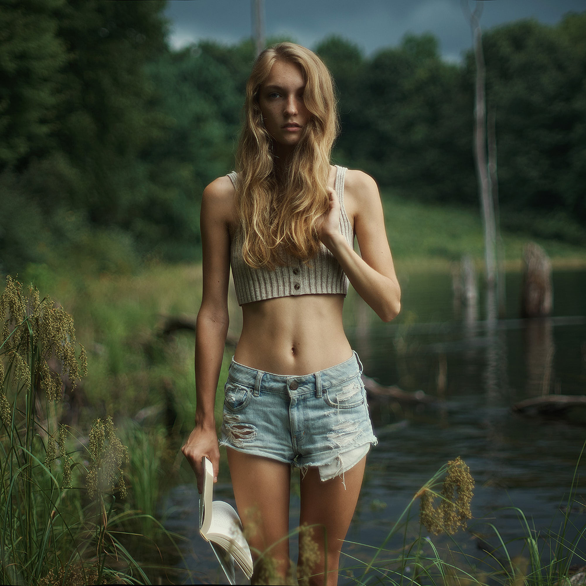 Beautiful slim half dressed young girl in jeans shorts holding a book. Editorial photoshoot on New Jersey lakes.