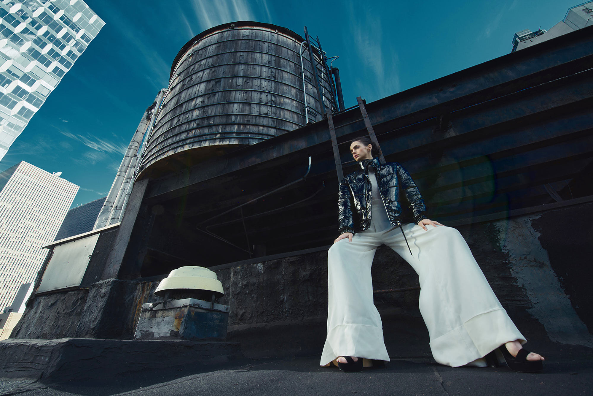 Mexican model in white pants and black leather coat on top of New York City roof with a great view. Fashion editorial photoshot.