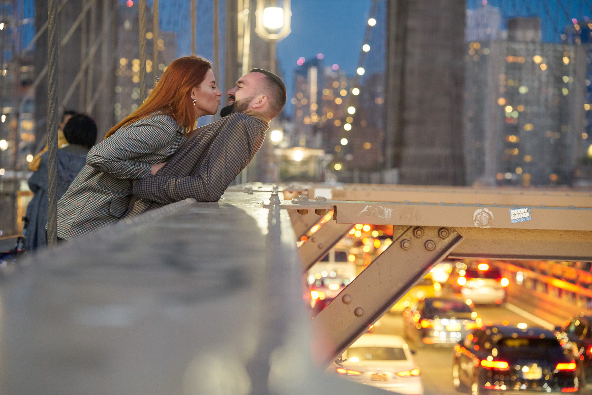 Brooklyn Bridge evening engagement photoshoot featuring a couple leaning over the bridge and enjoying the view of the car traffic below.