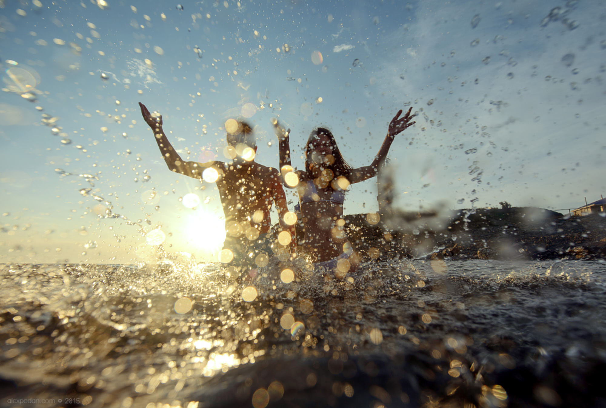 Destination beach engagement photography capturing playful moments of a happy couple throwing water drops at the camera during sunset in South Hamptons, NY.
