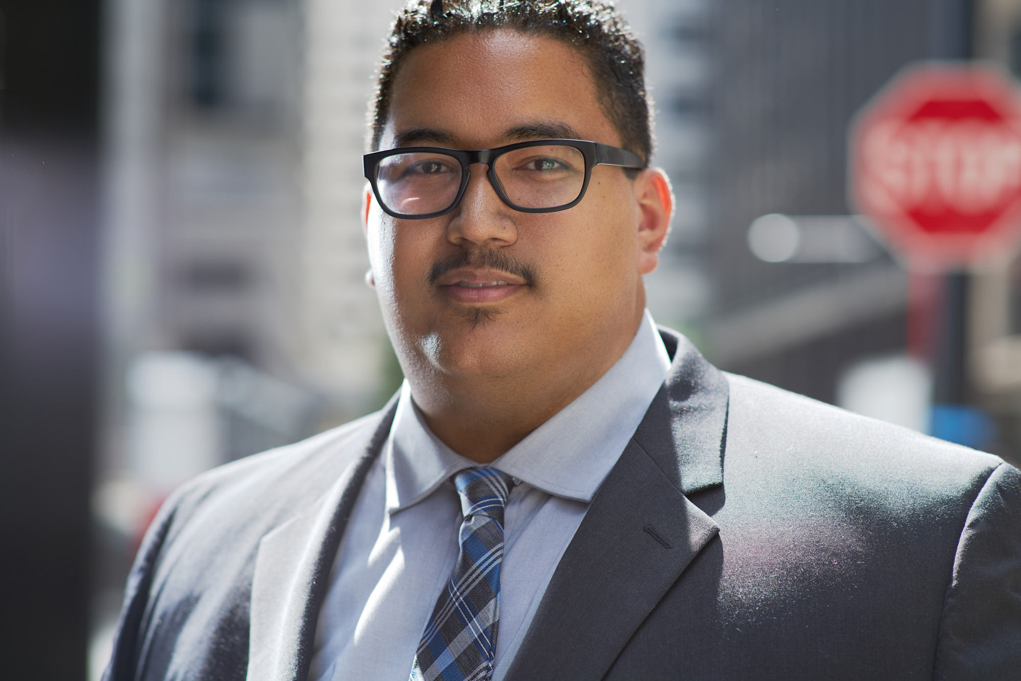 Corporate portrait of confident mixed race plus-size man in suit and glasses on New York City street.