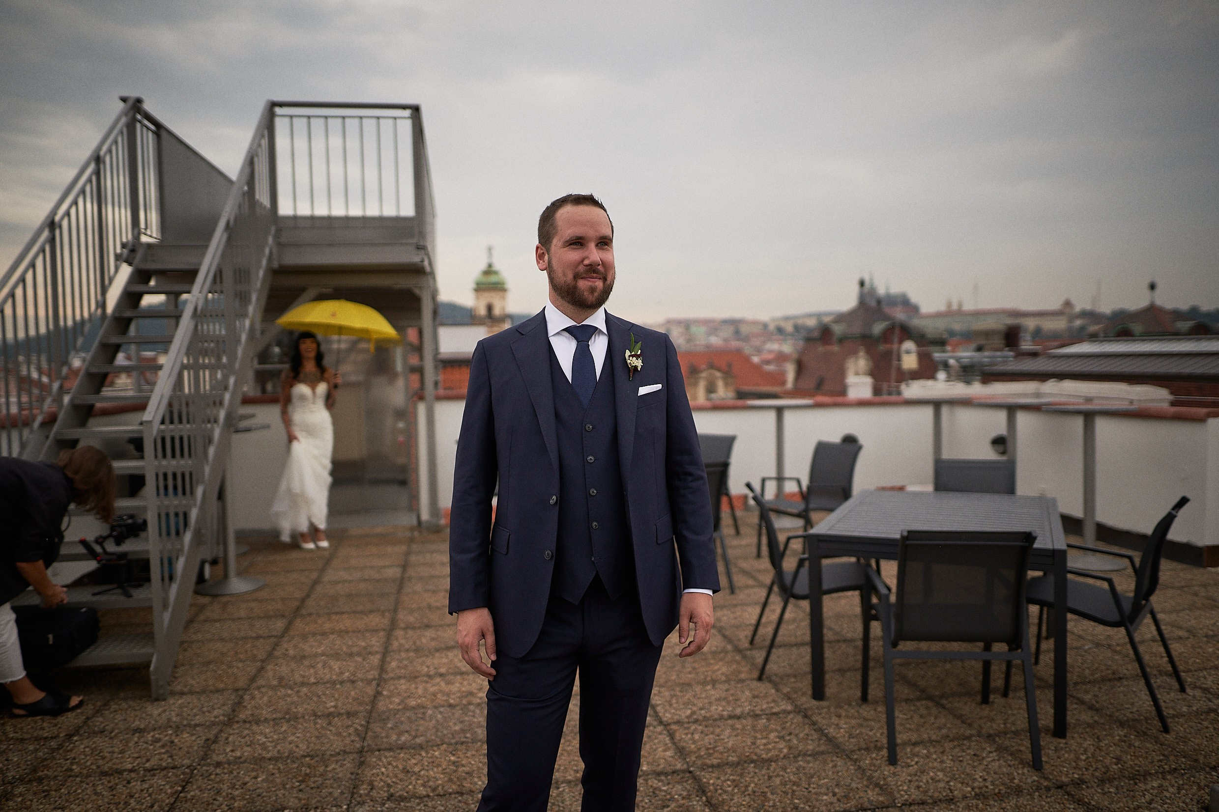 Tattooed bride approaching groom on rainy Prague rooftop first look.