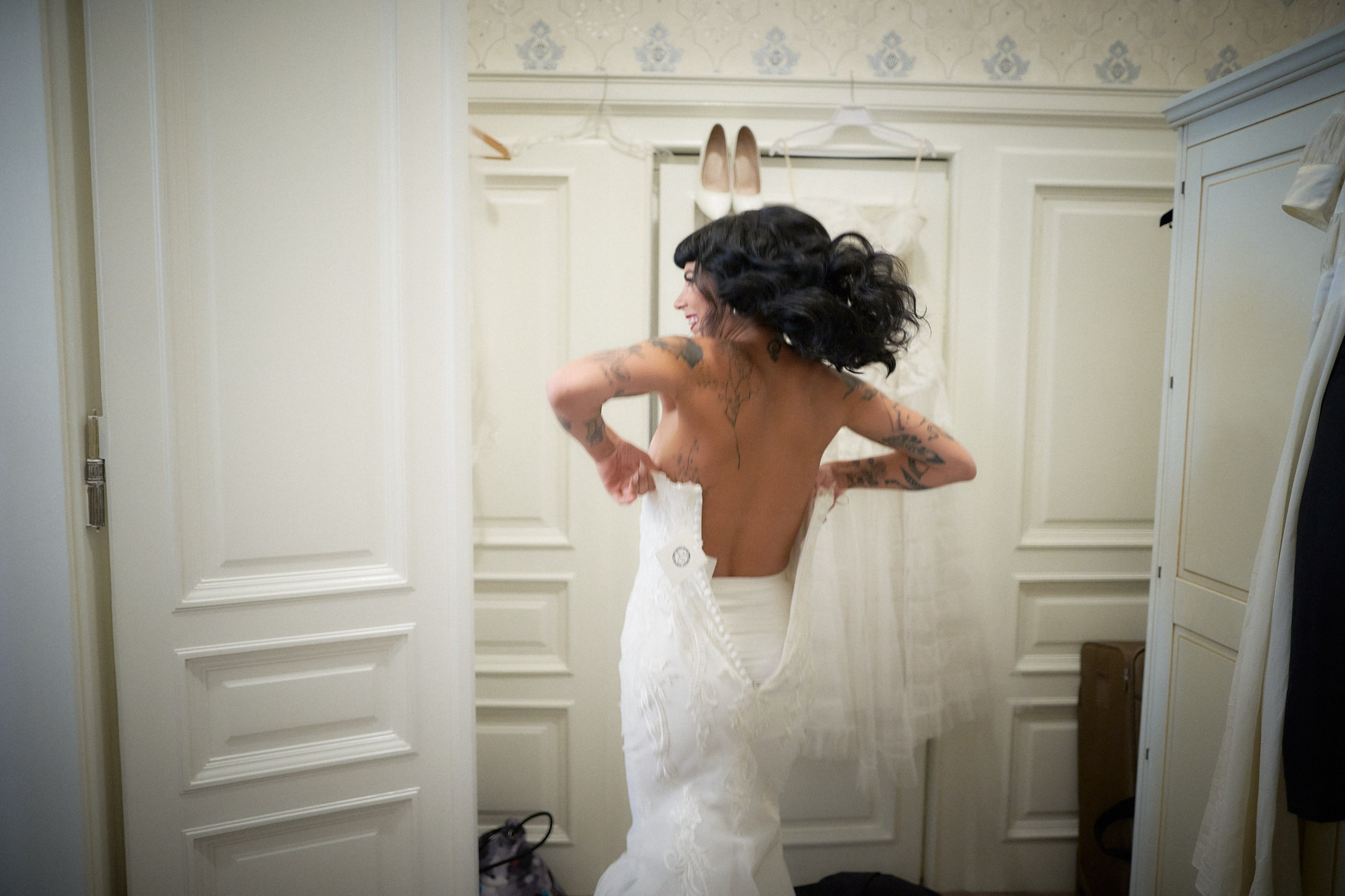 Bride laughing delightedly while slipping into gothic wedding dress.