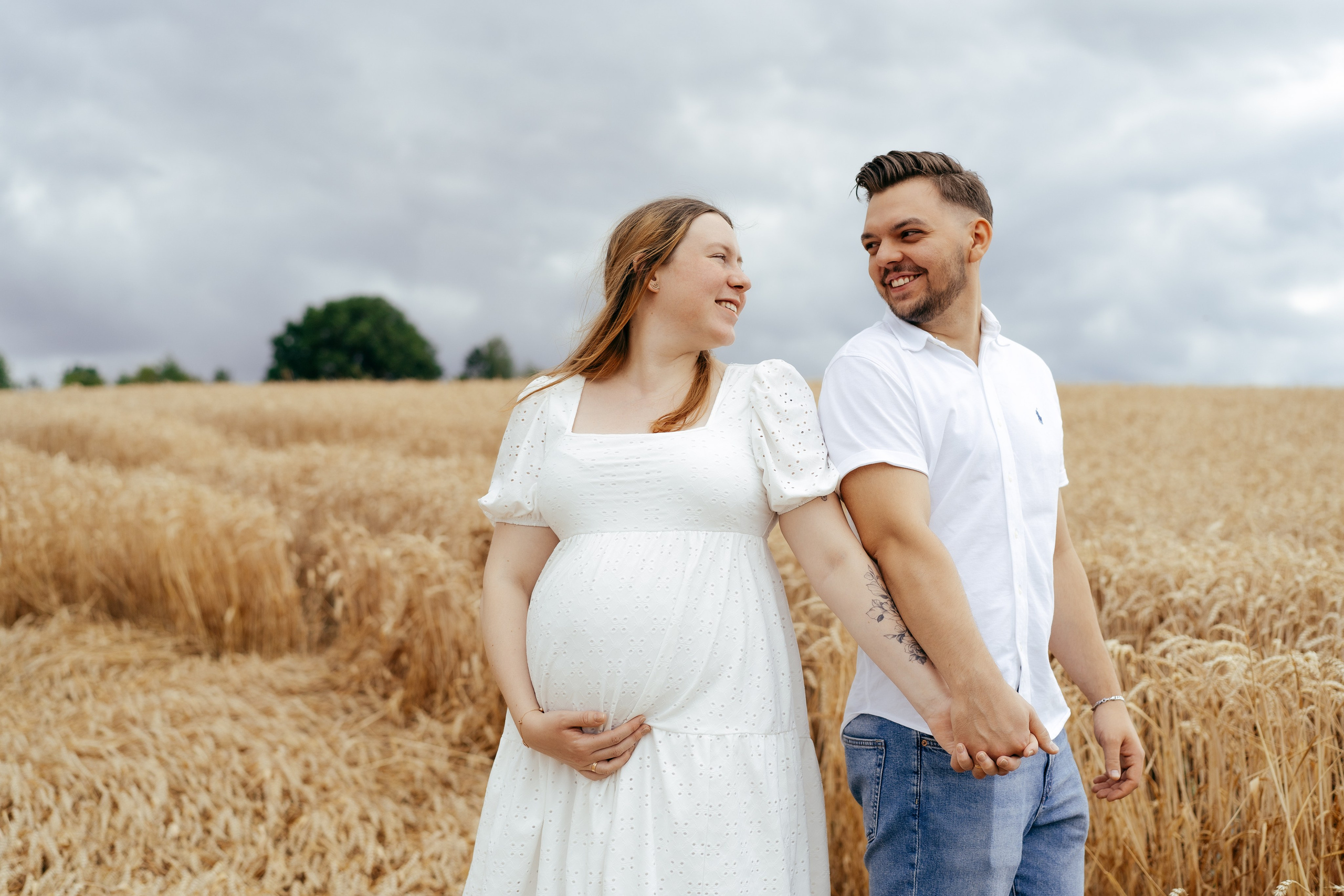 Schwangere Frau und ihr Partner posieren glücklich im Freien für ein Fotoshooting