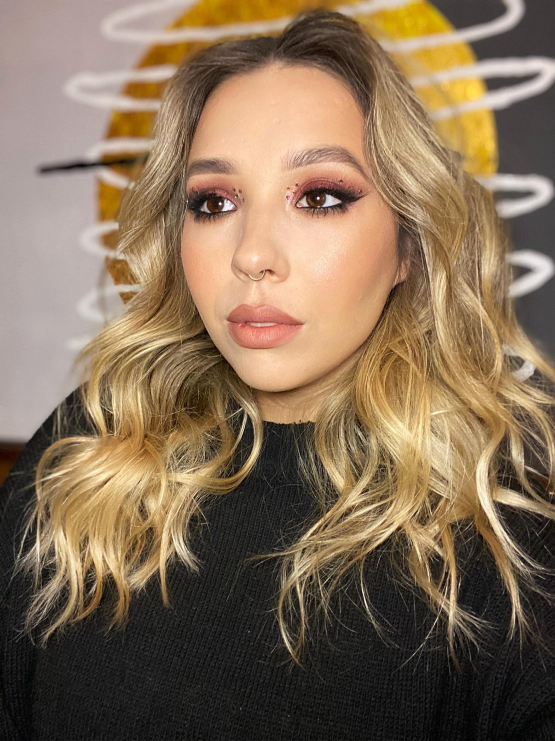 a blond woman with wavy hairstyle and dark red smoky eyes makeup and strasse on her eyes