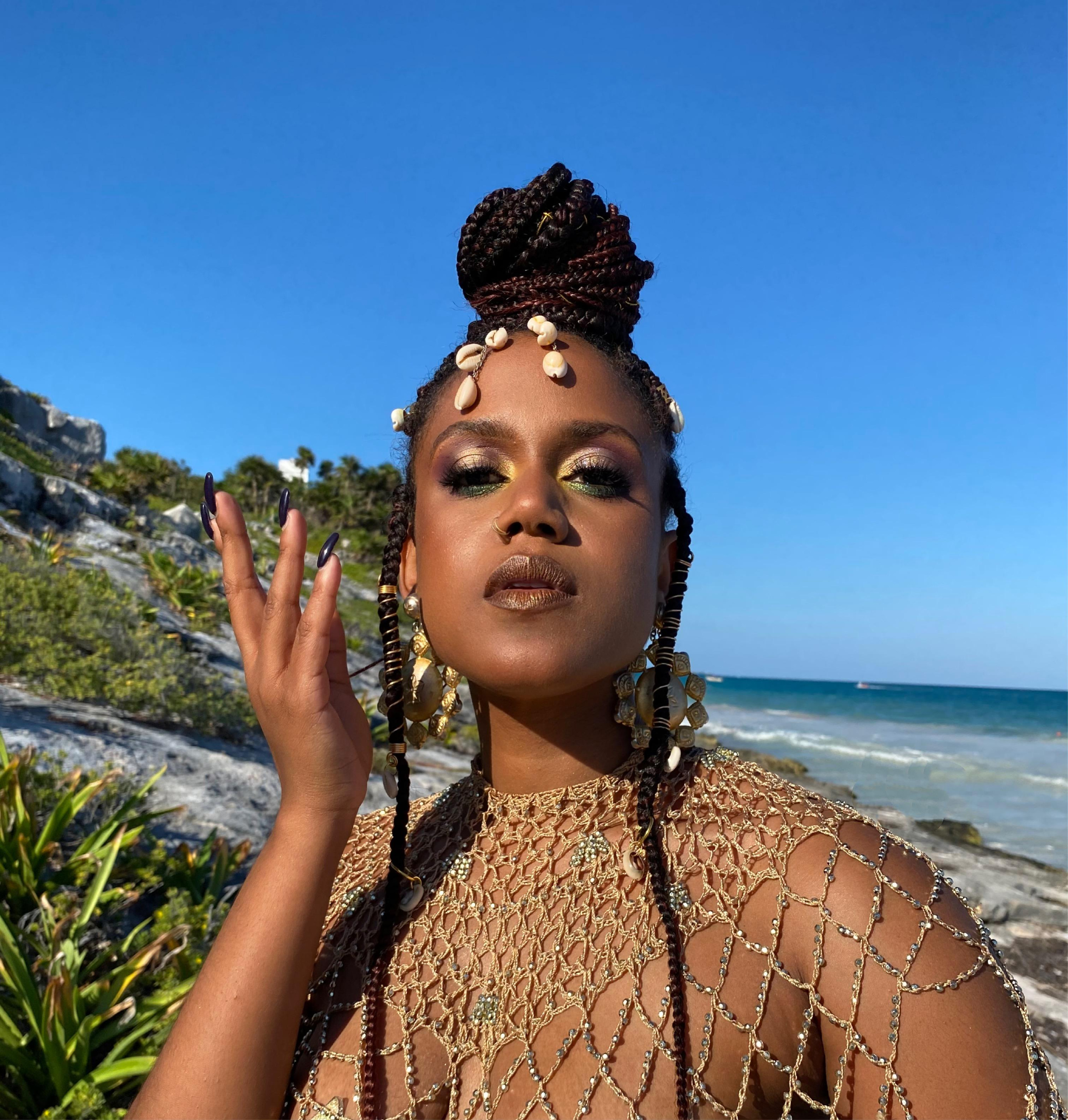african black woman with colorful artistic makeup posing next to the sea with shells in her hair