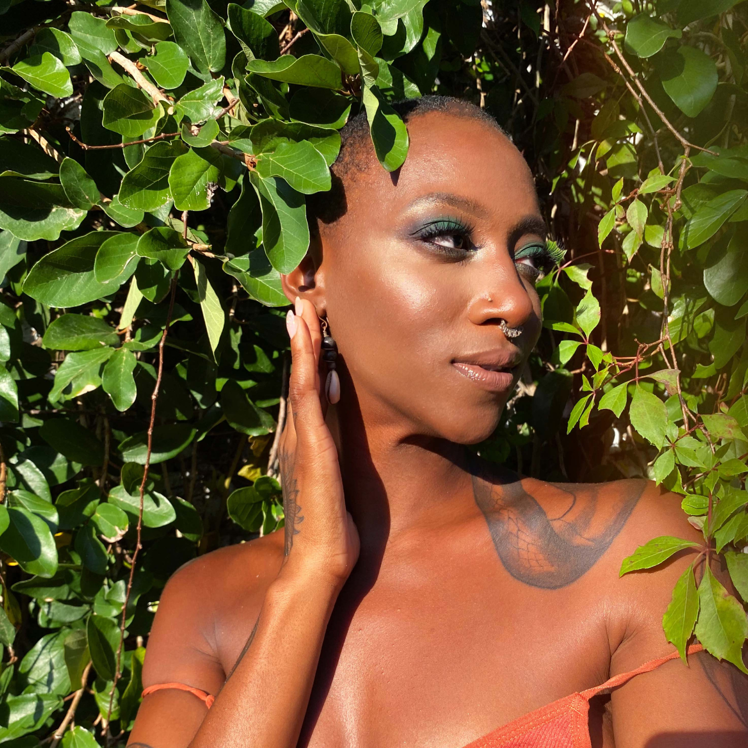 black girl with a snake tattoo posing in the green with green bright makeup on.