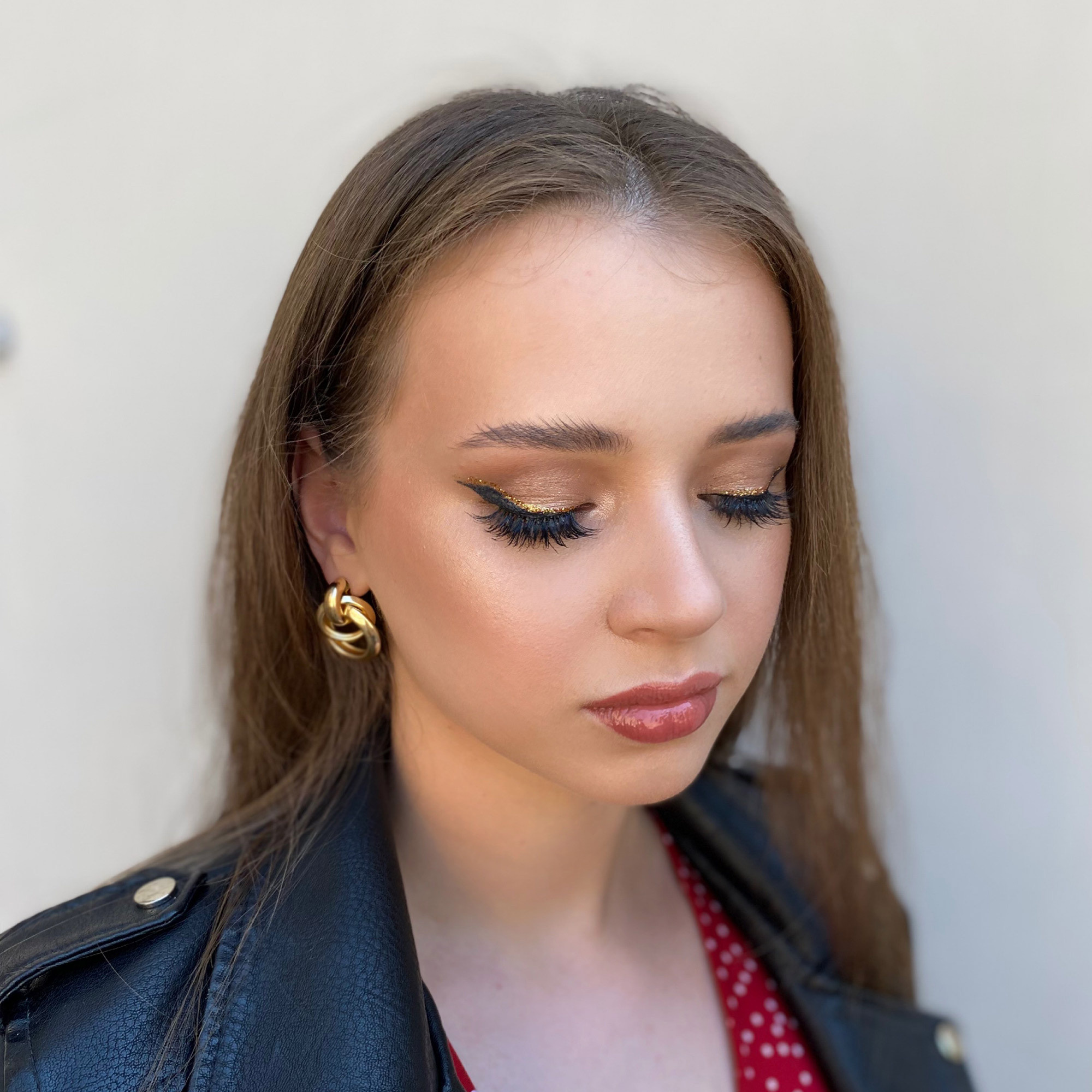 a white girl with sharp black and golden eyeliner with false eyelashes and glossy lips