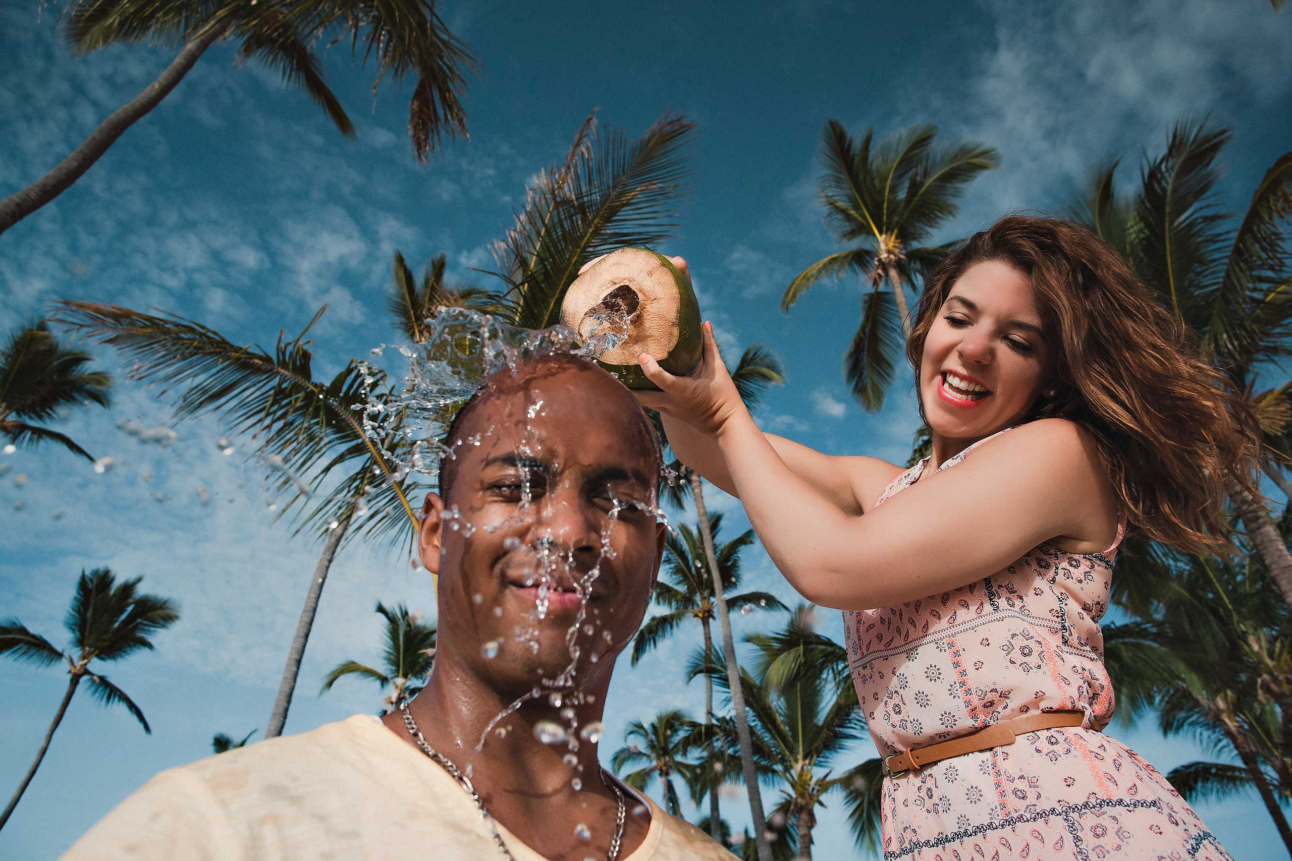 red hair lady is spilling coconut milk on a her bold boyfriend with palm trees on a background