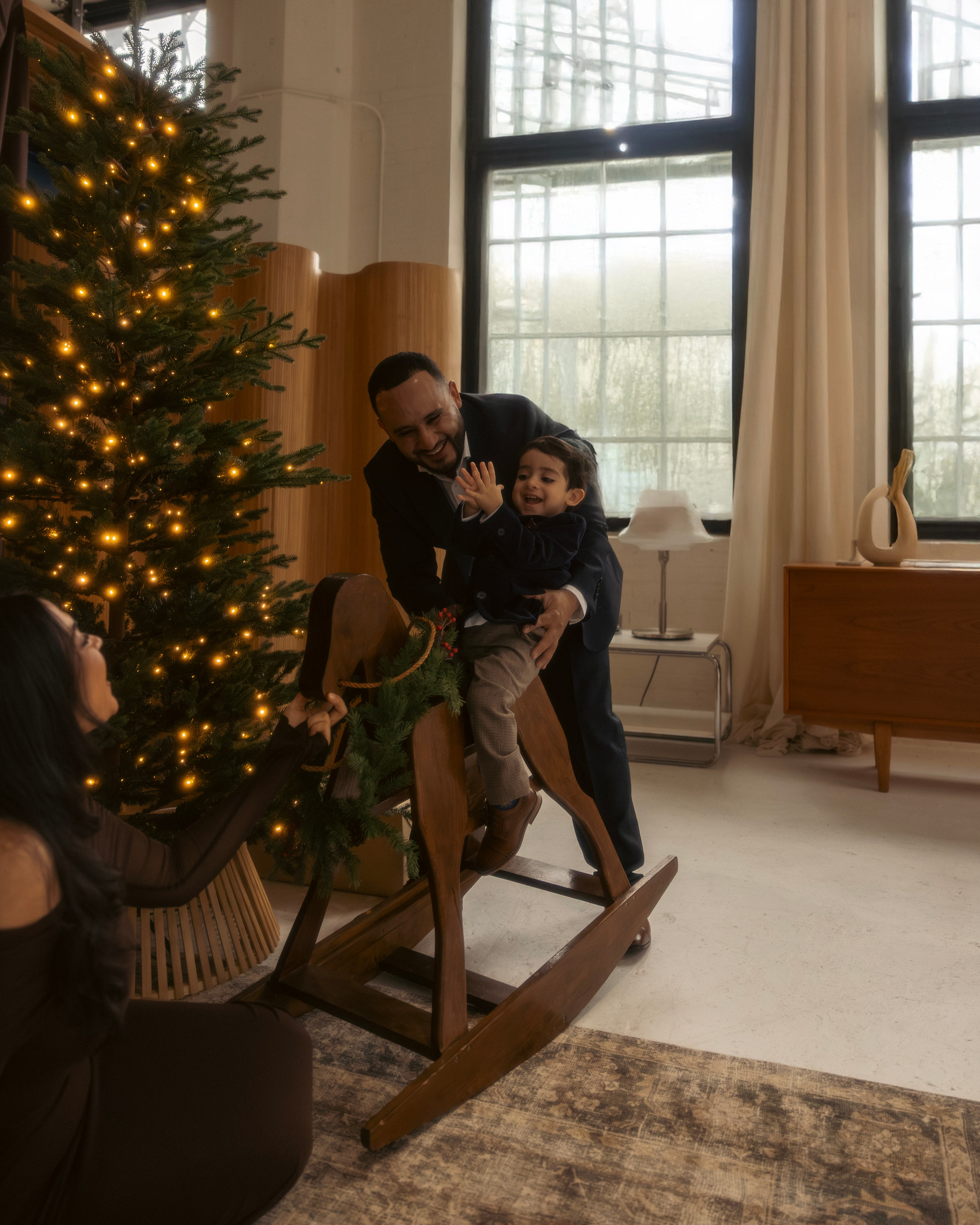 Parents kissing child near Christmas tree during holiday shoot