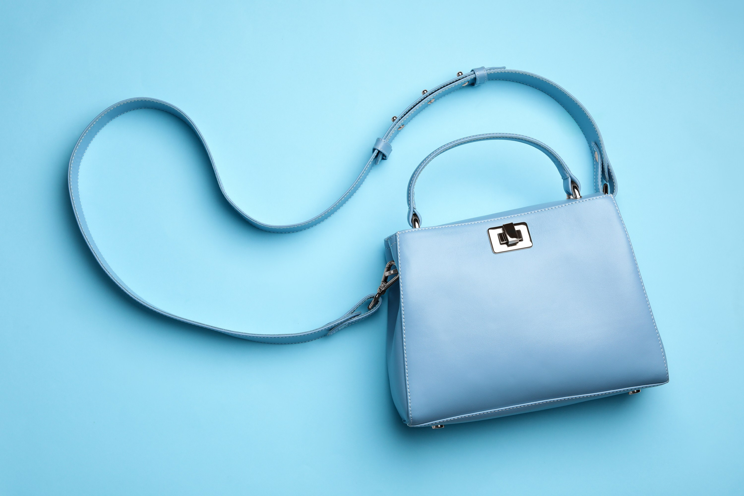 Top view of a stylish blue purse with a twisted strap against a solid blue surface