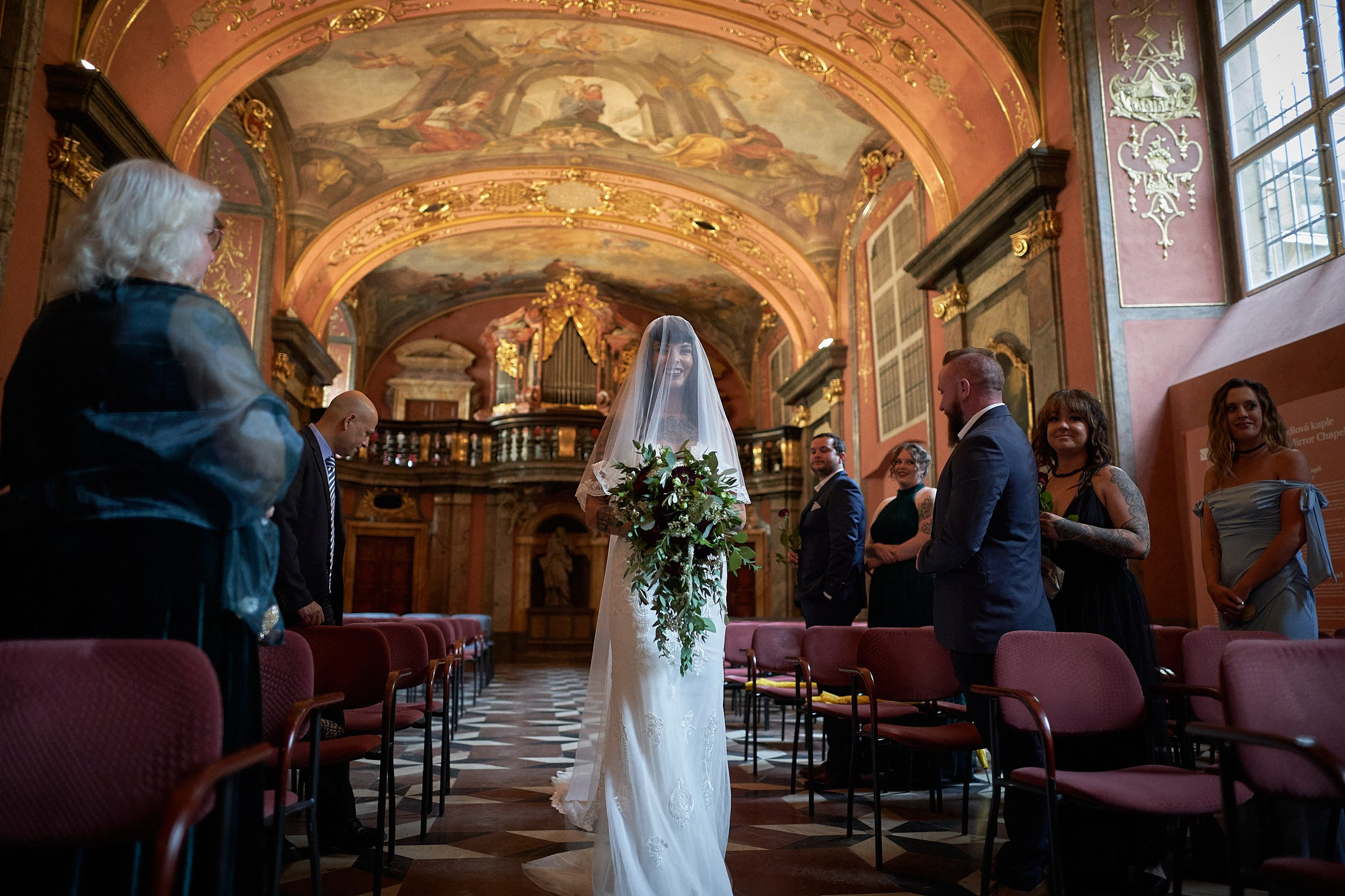 Bride entering ornate Klementinum Mirror Chapel for gothic ceremony.